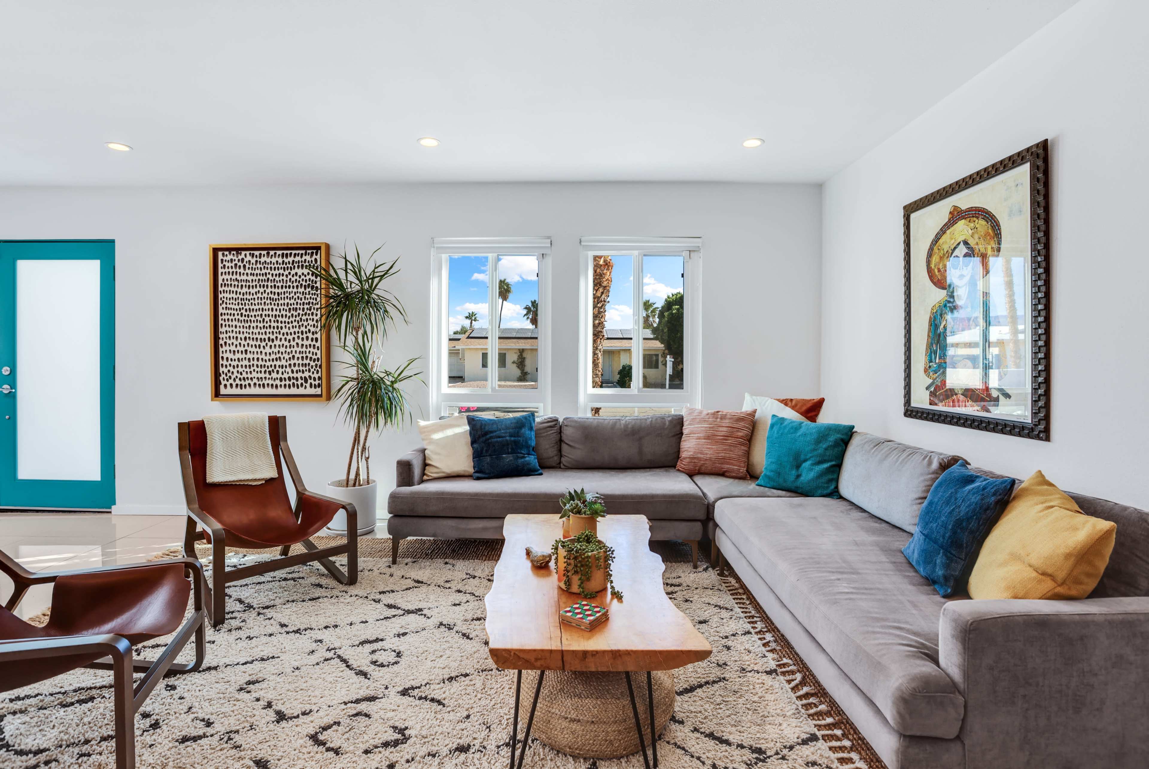 The living room features a sectional sofa, a wooden coffee table, a patterned rug, and large windows with palm trees visible outside.