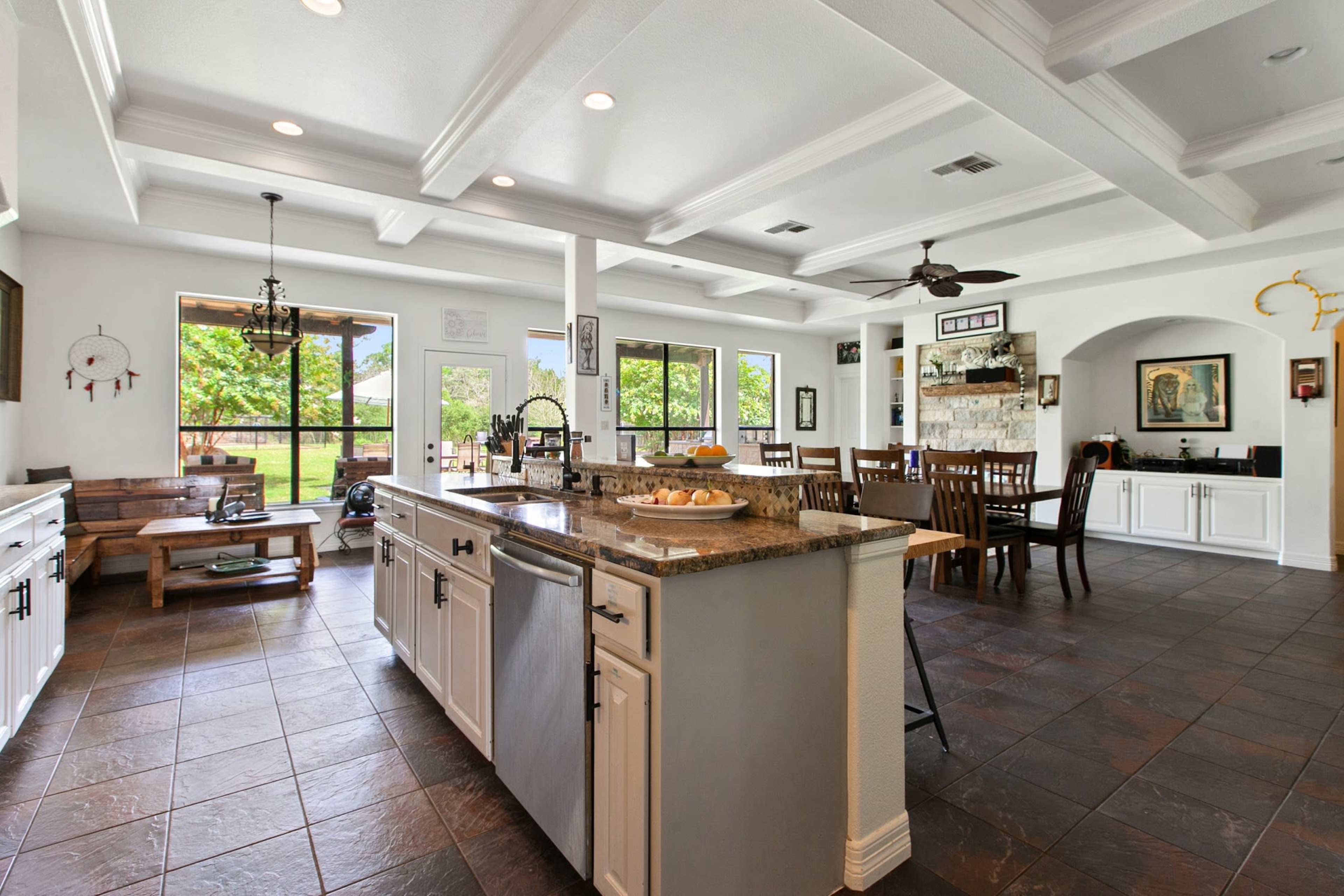 A spacious kitchen and dining area featuring white cabinetry, a central island with granite countertops, and large windows overlooking a green landscape.