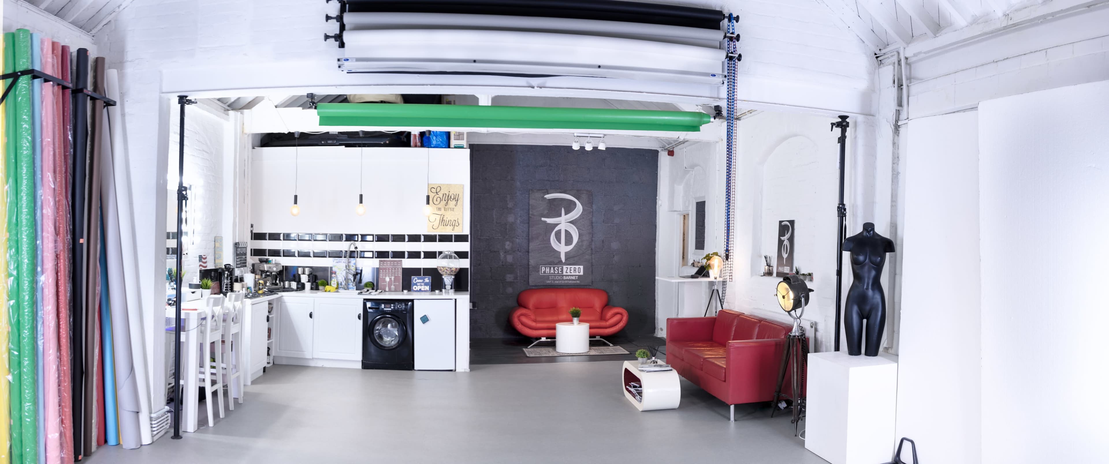 A spacious studio apartment with a kitchenette on one side, a red couch, a washing machine, and a mannequin in the corner.