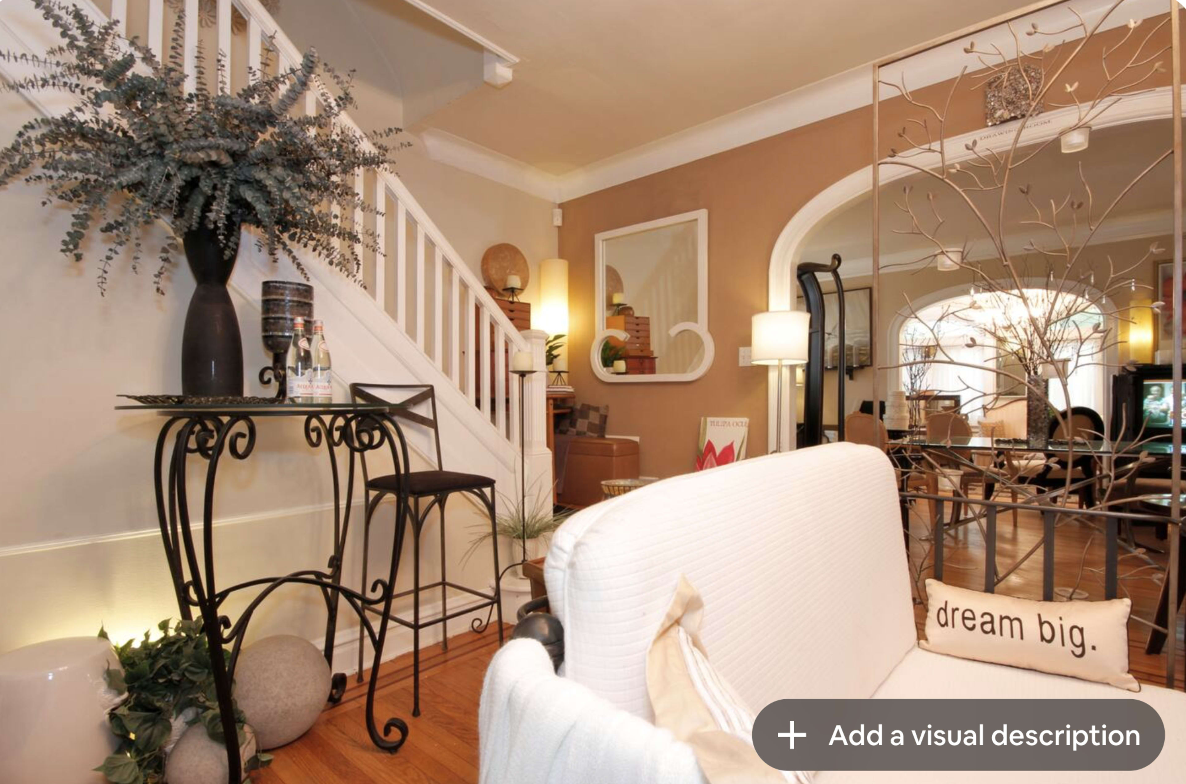 The image shows a cozy, well-decorated living space featuring a staircase, a decorative metal table, and various plants.