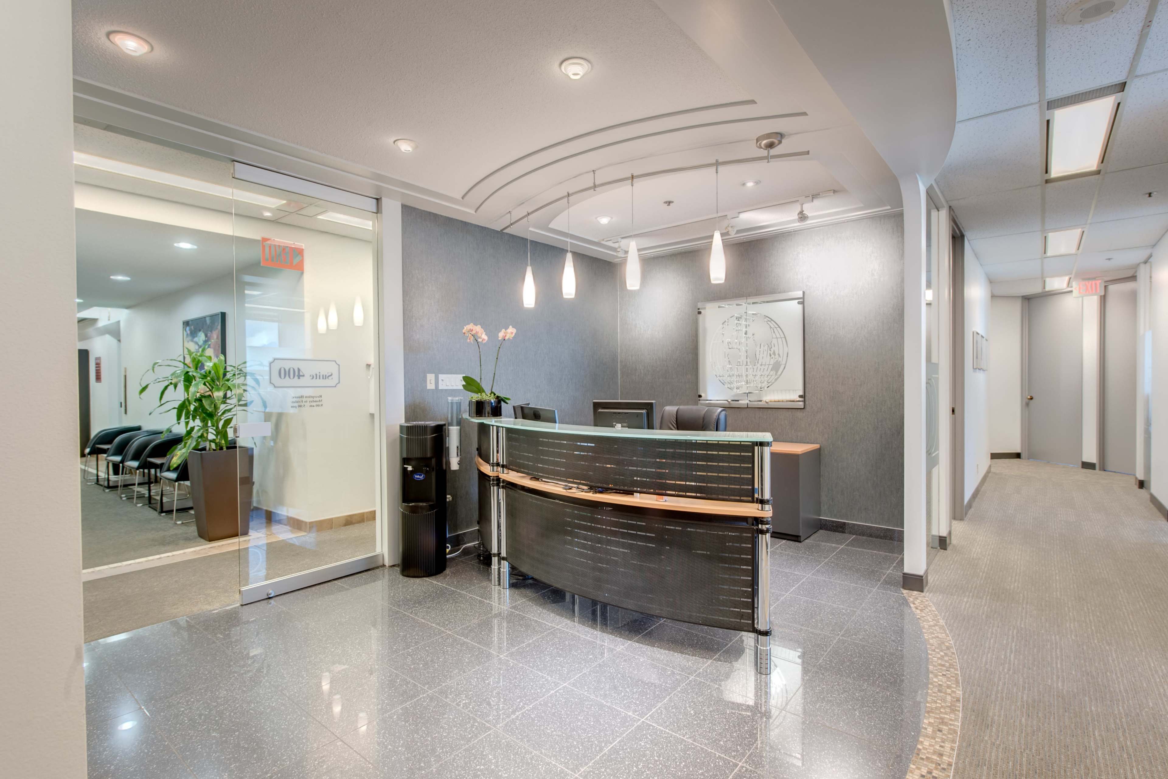 A modern office reception area with a curved desk, a decorative plant, and a waiting area with black chairs.