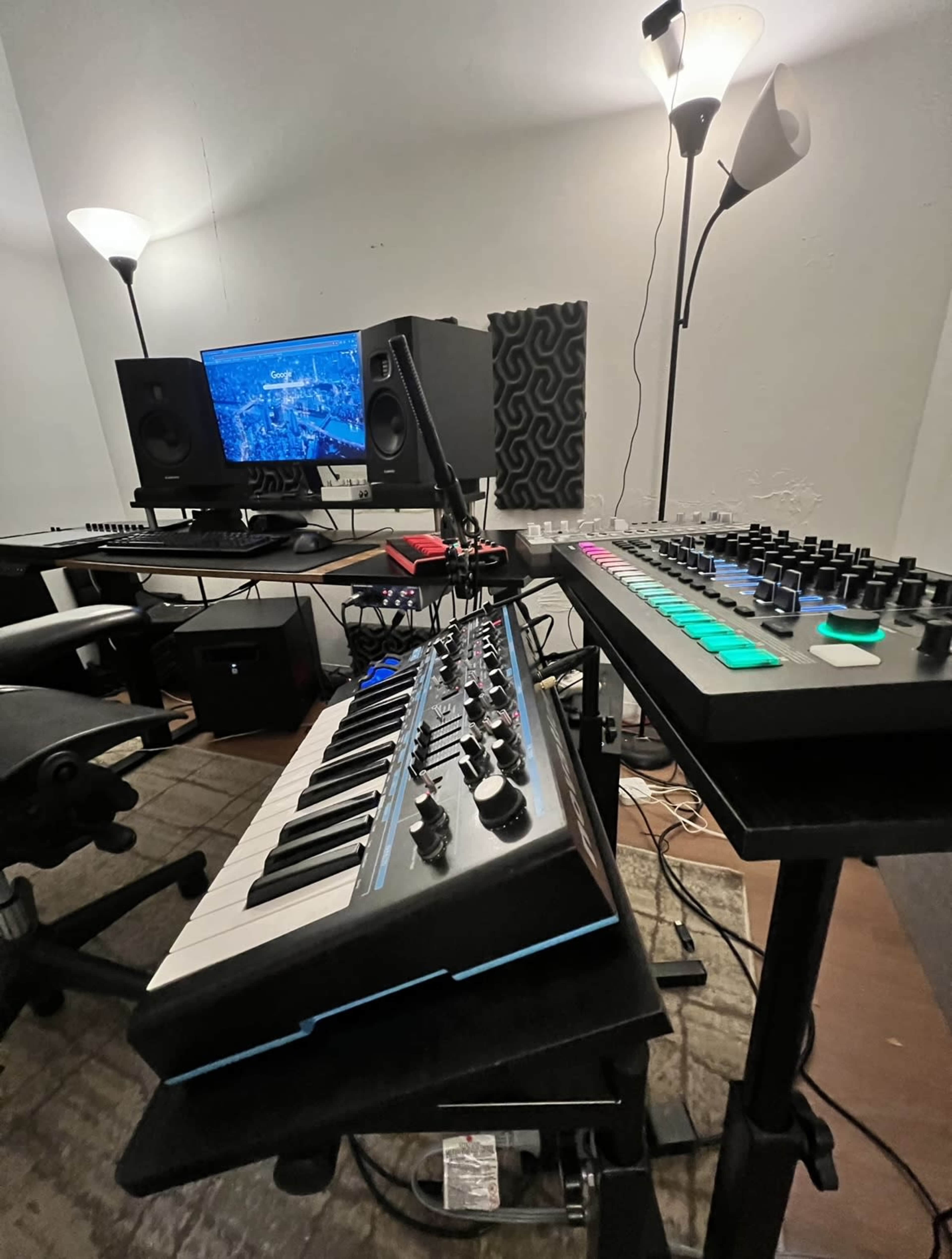 A home music production setup features a keyboard, a synthesizer, dual studio monitors, and a computer screen displaying music software.
