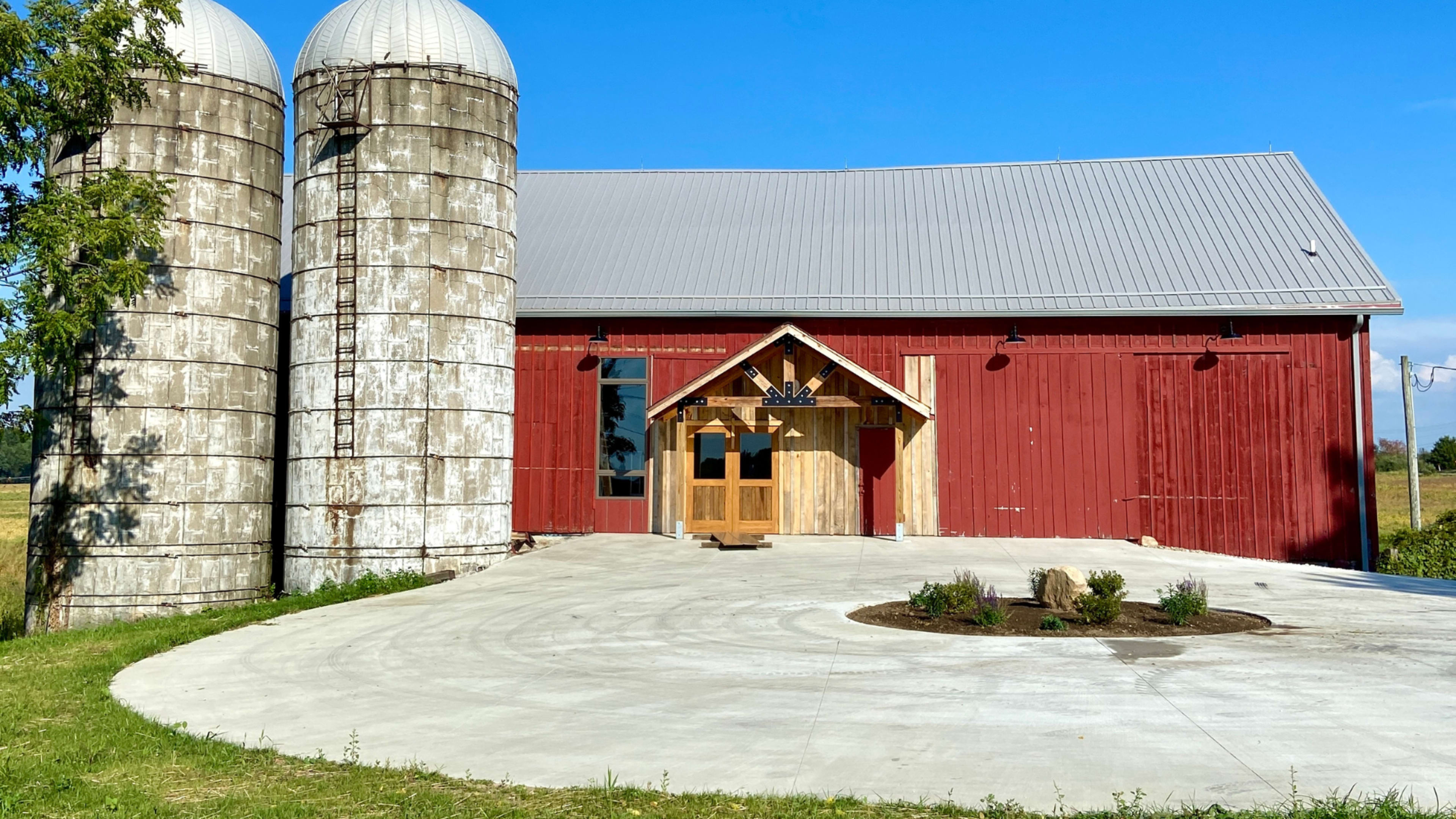 A red barn features two cylindrical silos, with a concrete pathway leading to a wooden entrance.
