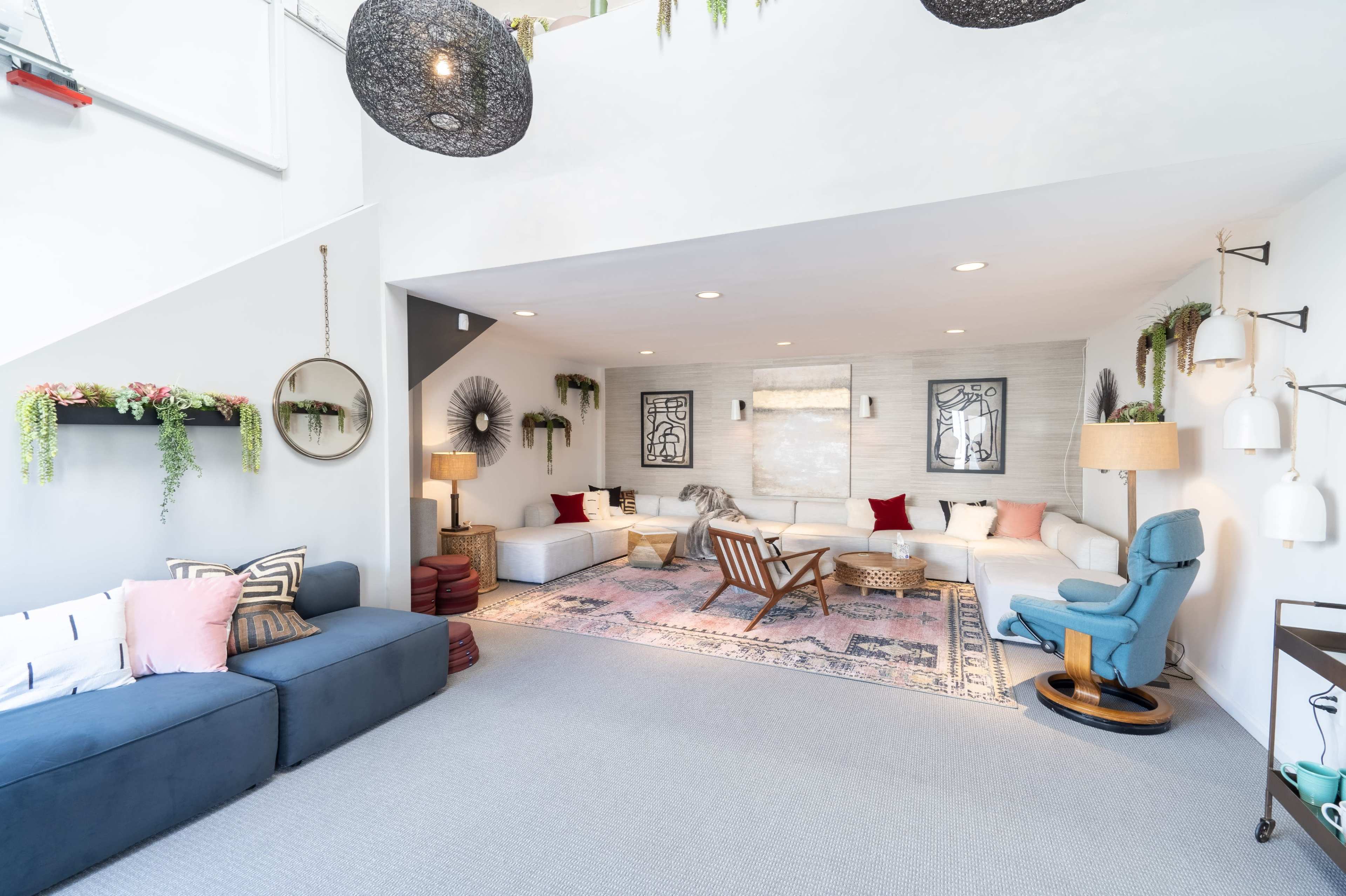 A modern living room area with a sectional sofa, decorative wall art, and various lighting fixtures arranged around a central rug.