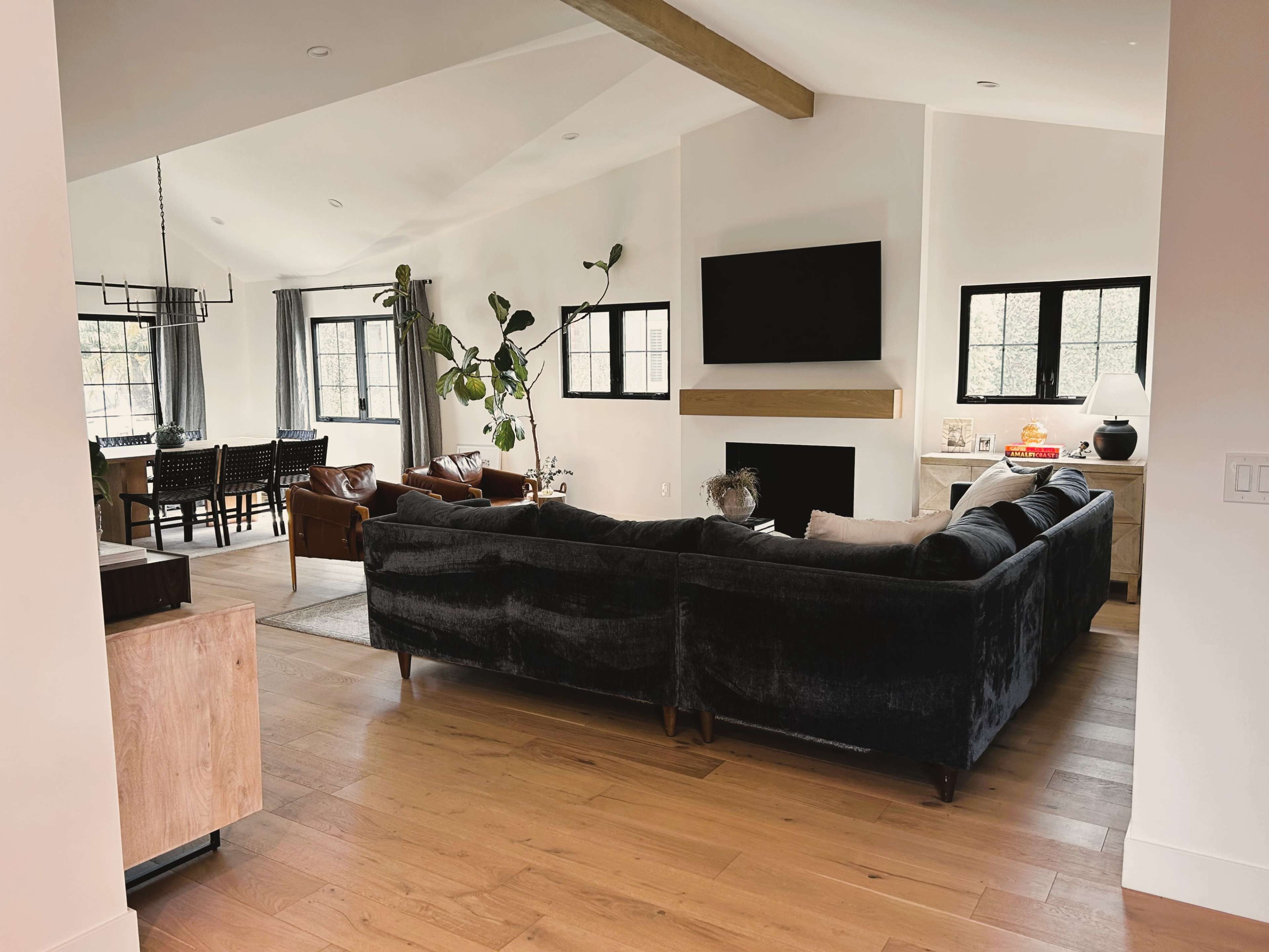 A modern living room with a dark sectional sofa, a fireplace, and a view of a dining area through an open space.