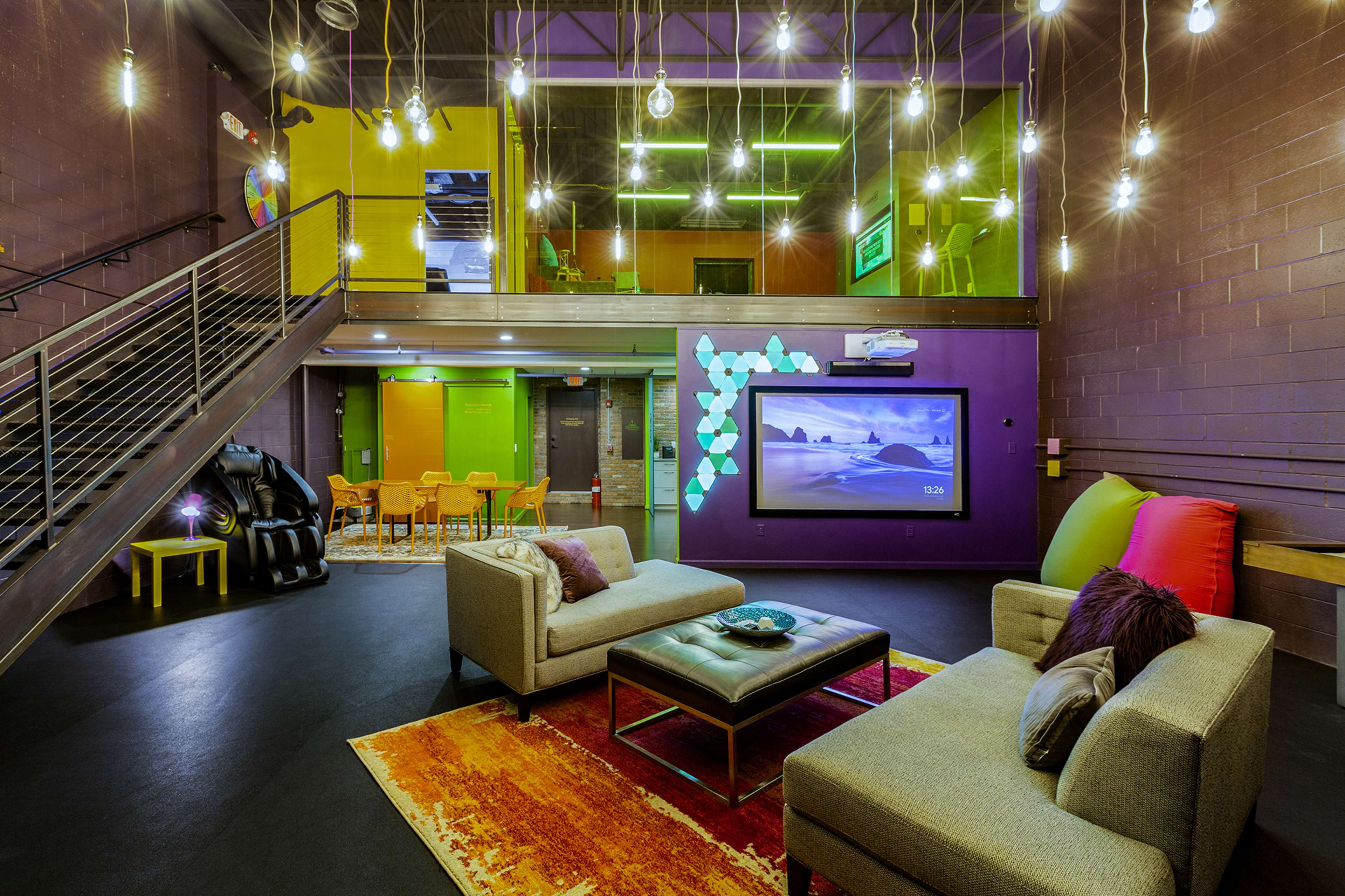 A modern lounge area with two sofas, a coffee table, and a large television, surrounded by bright lighting and vibrant colored walls.