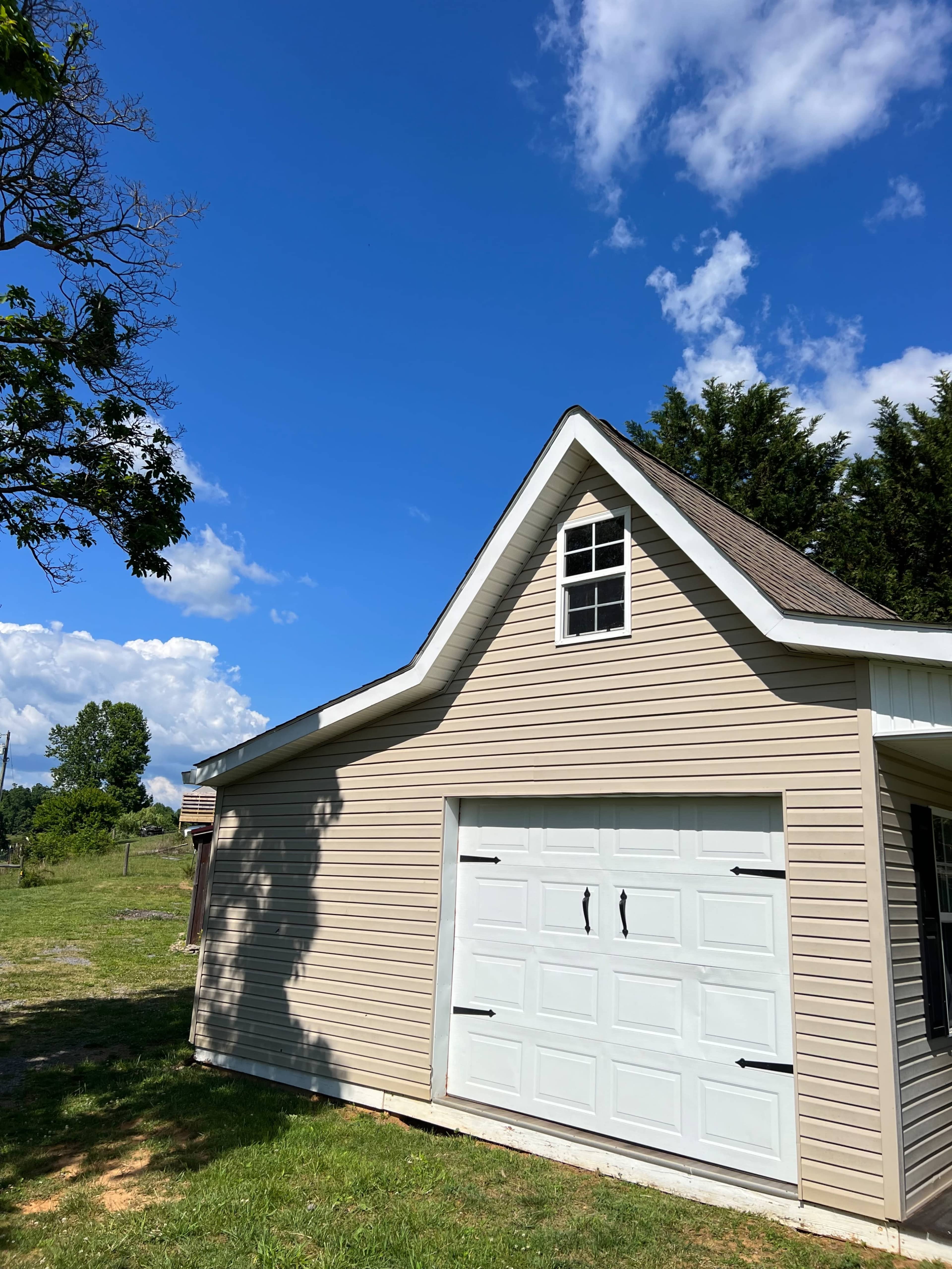 A light-colored garage with a peaked roof is situated next to a grassy area under a blue sky with scattered clouds.