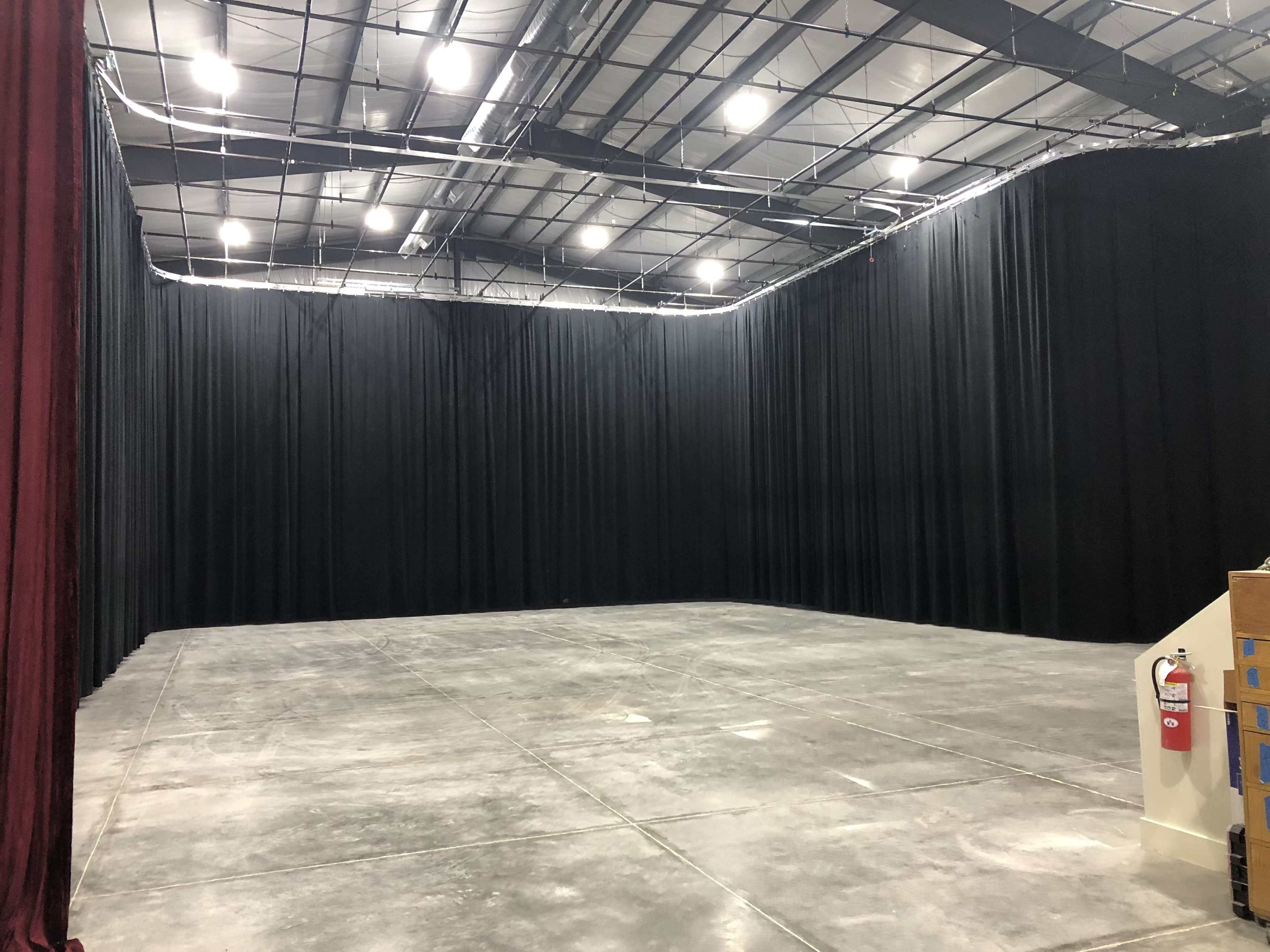 A large studio space with black curtain walls, a concrete floor, and overhead lighting.