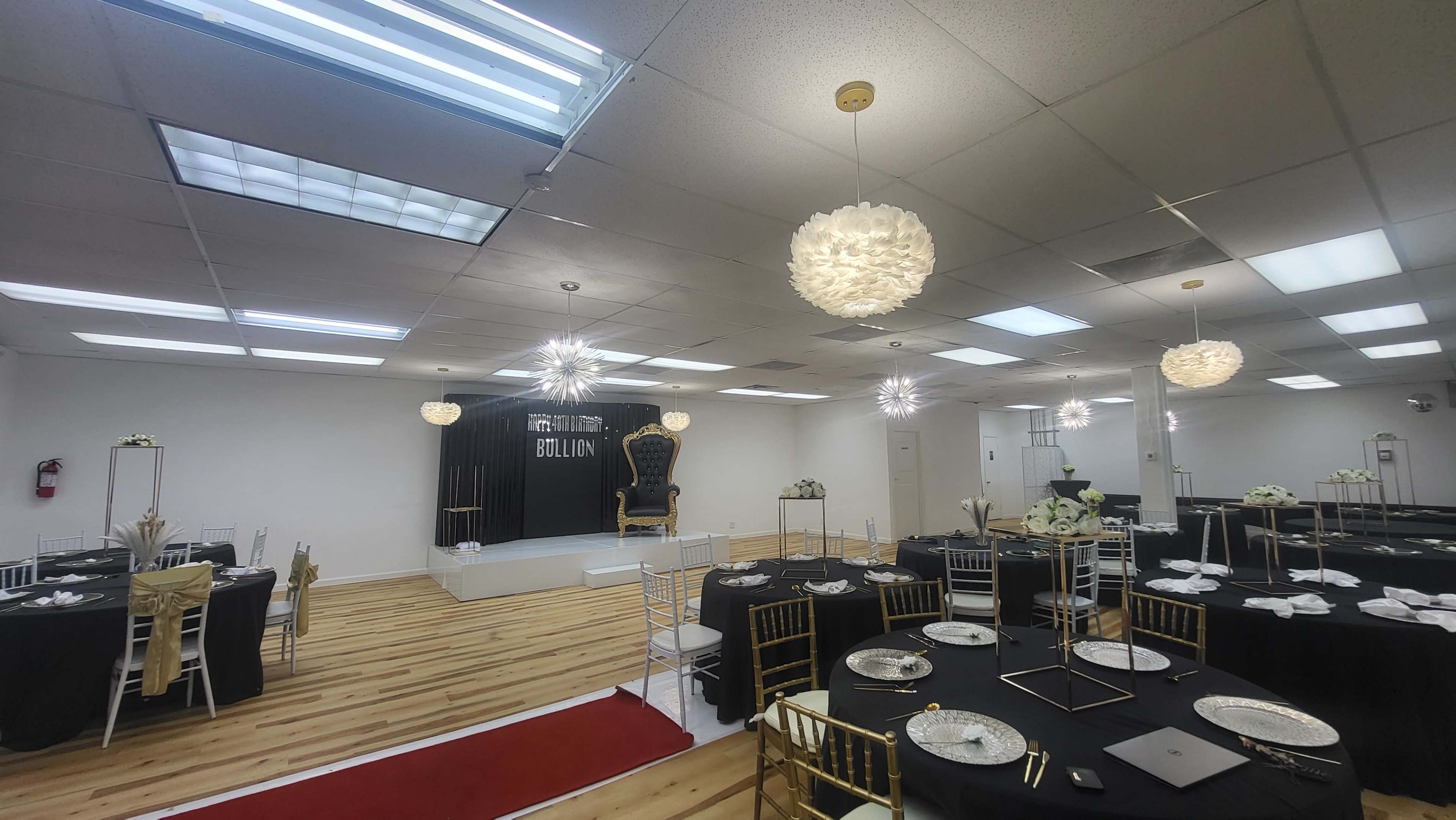 A decorated event space with black and gold tables, elegant light fixtures, and a prominent stage area.