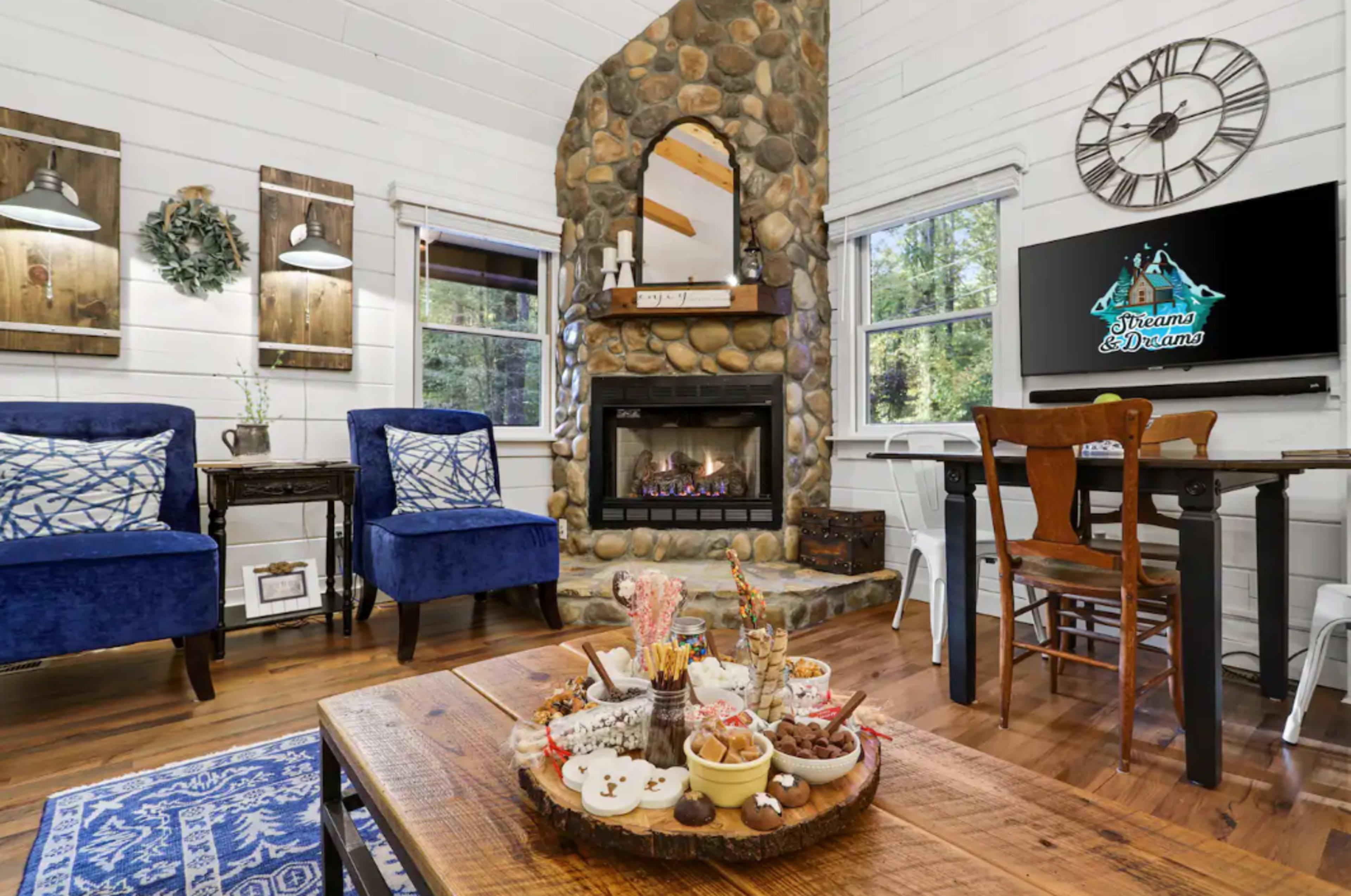 A cozy living room featuring a stone fireplace, wooden furniture, and blue upholstered chairs.