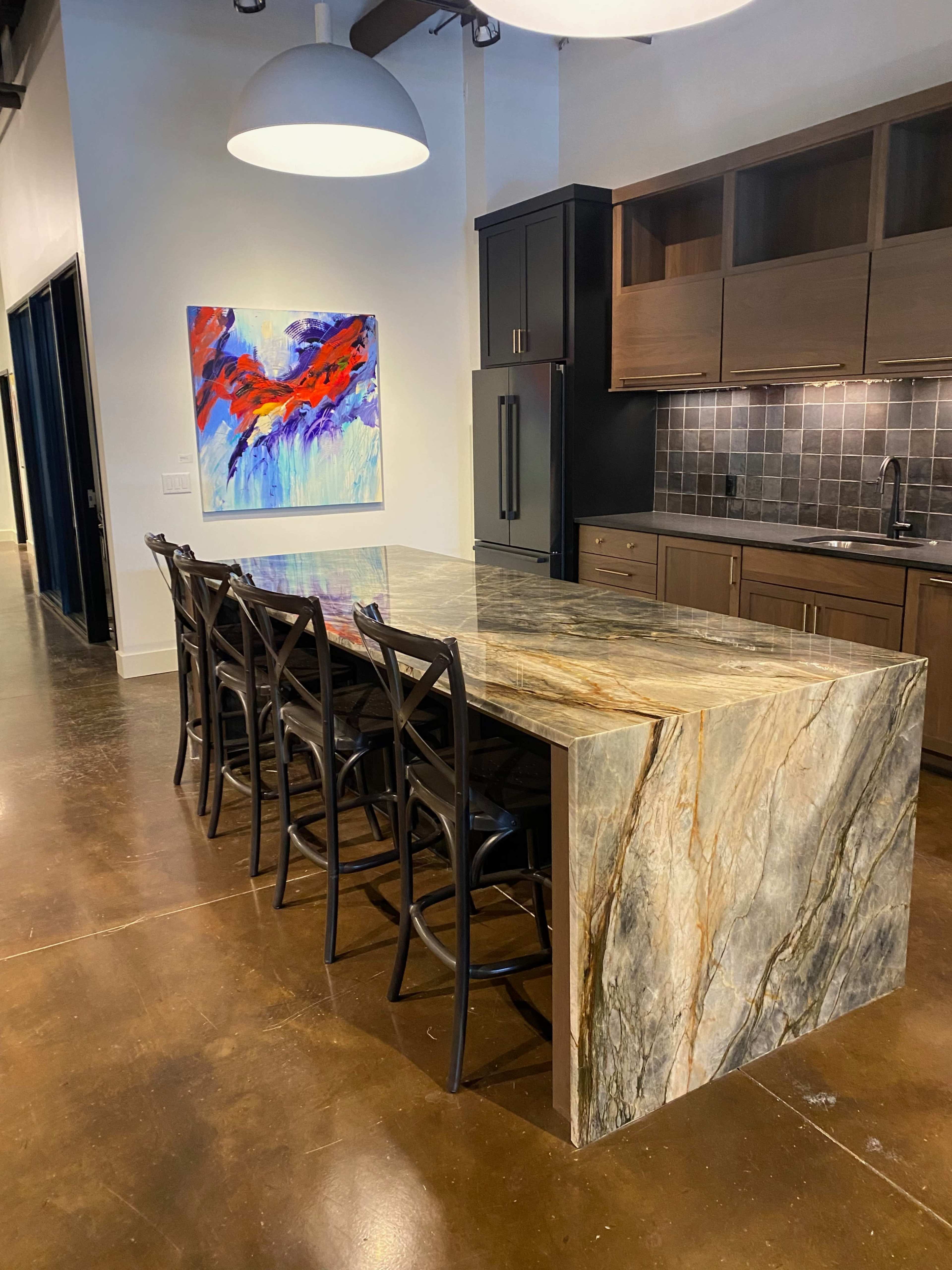 A kitchen features a large, multicolored stone island with bar seating and modern cabinetry in the background.