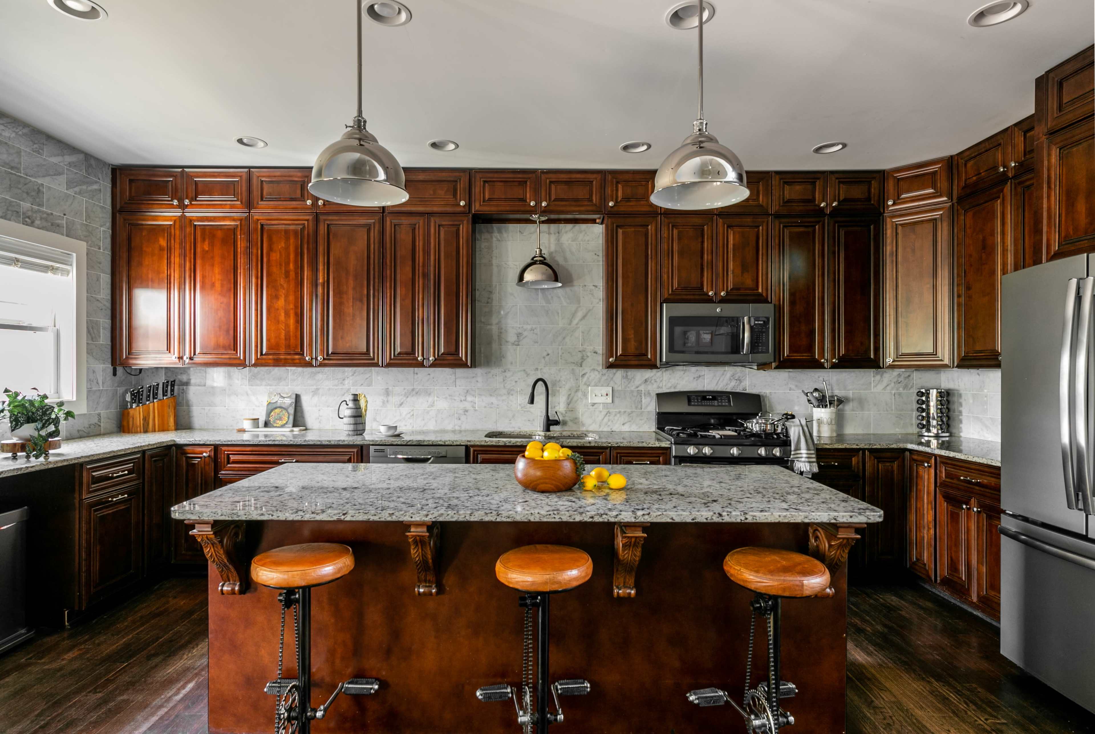 The modern kitchen features dark wood cabinets, a granite island with seating, and stainless steel appliances.