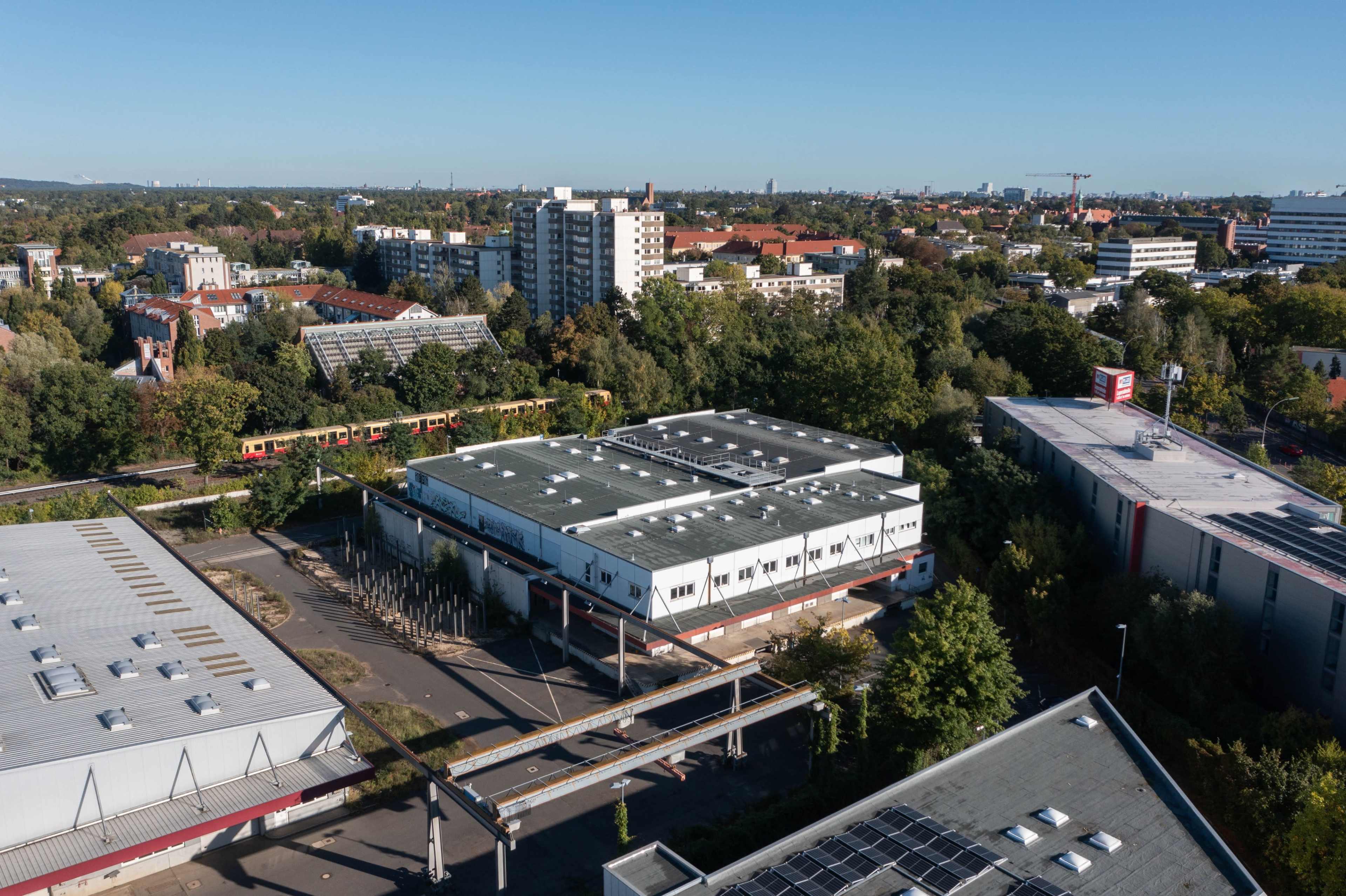 The image shows a view of a cityscape featuring multiple buildings, including residential and commercial structures, with a railway line visible in the foreground.