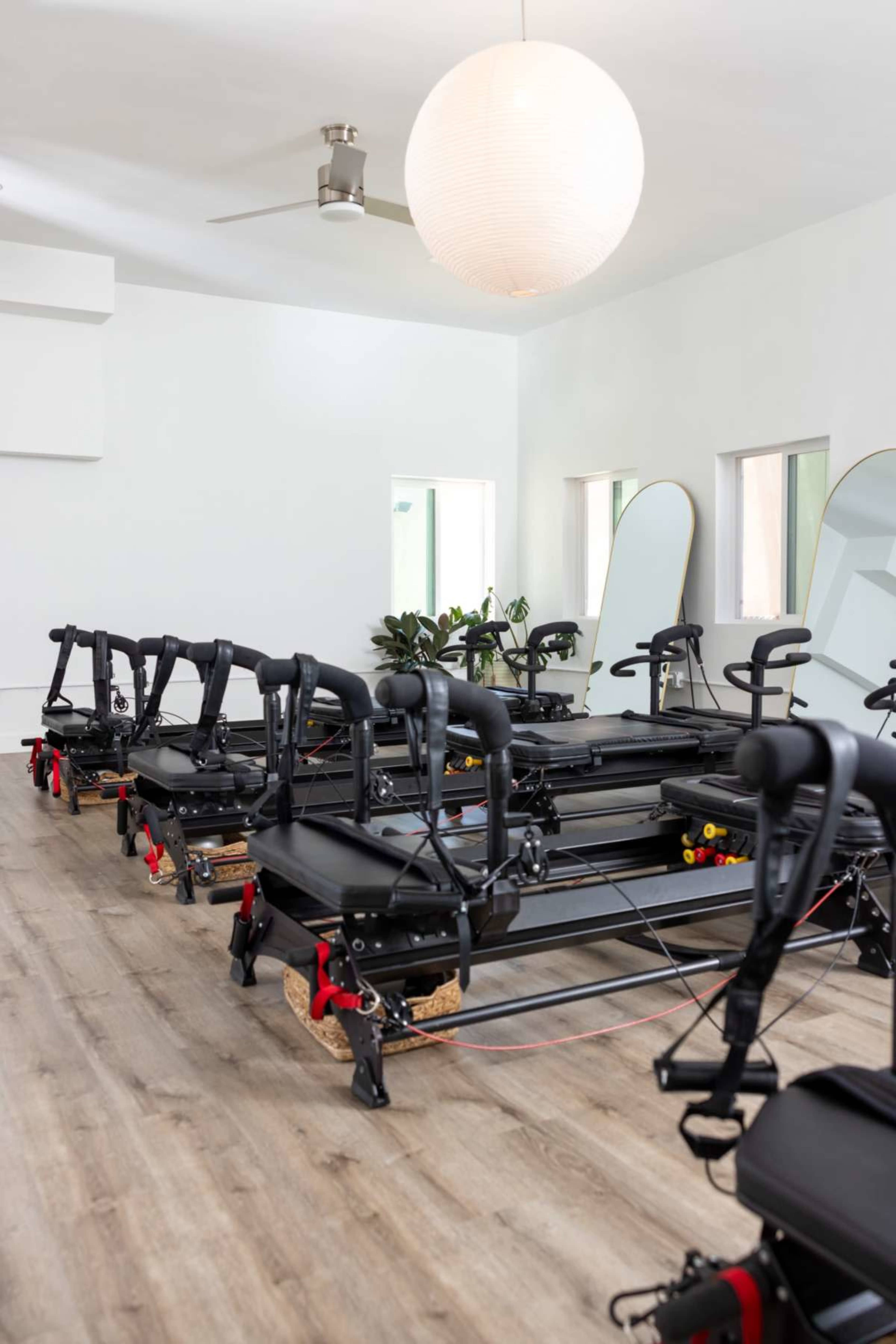 The image shows a fitness studio featuring several reformer machines arranged in rows on a wooden floor.