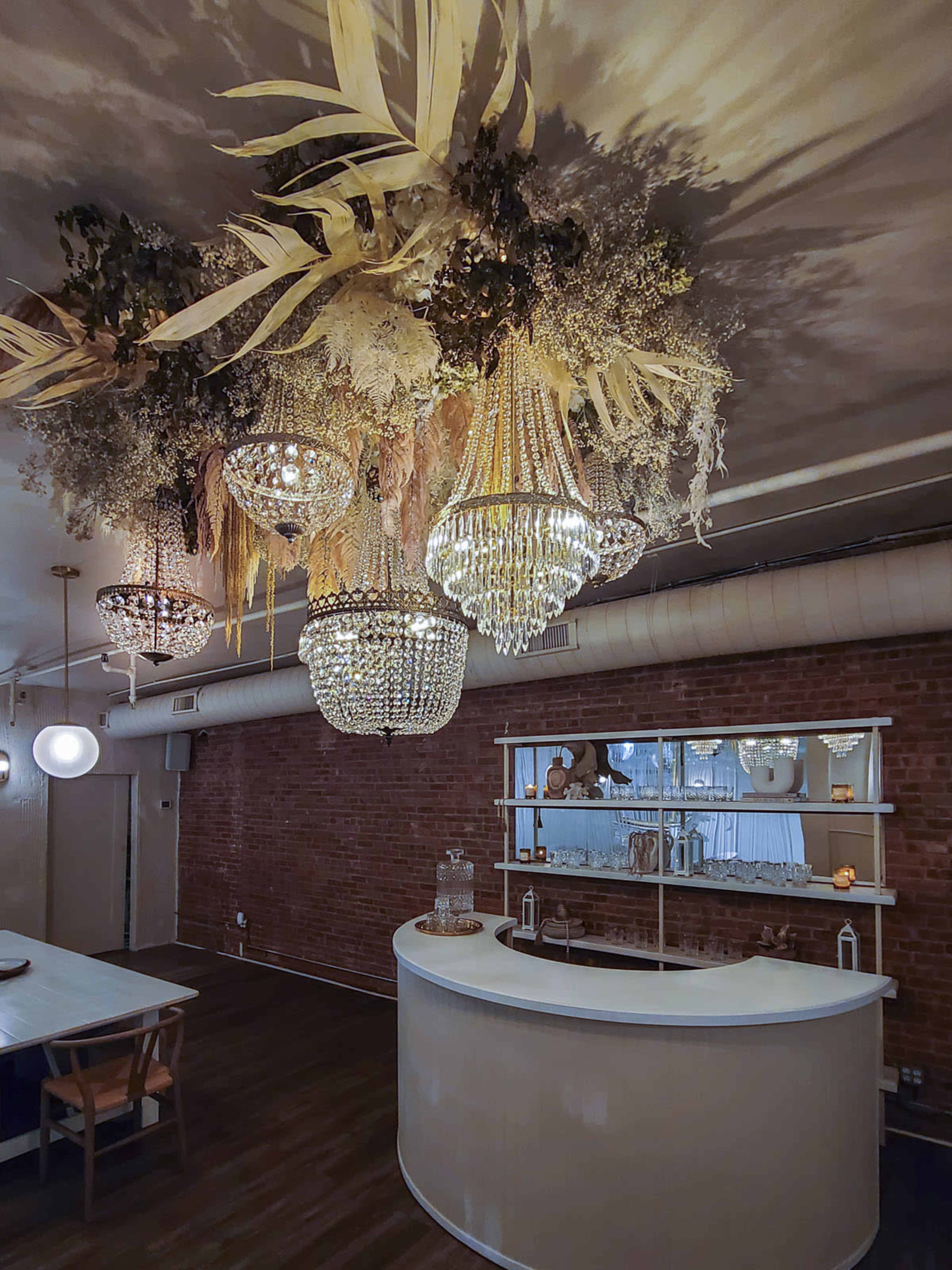 A bar area with a white curved counter and an ornate ceiling adorned with chandeliers and dried floral arrangements.