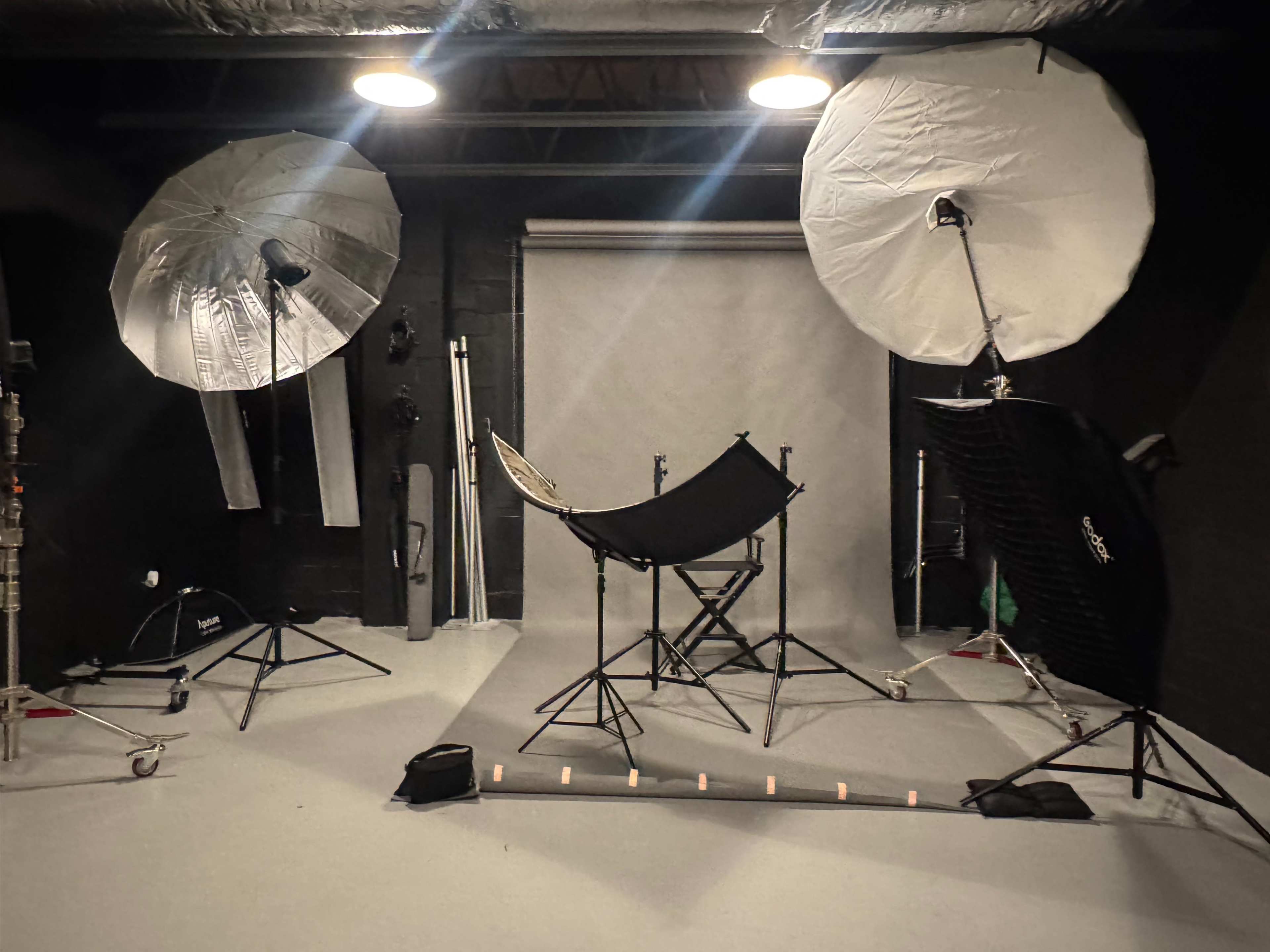 The image shows a photography studio equipped with two large softbox lights, a backdrop, and various props arranged on the floor.