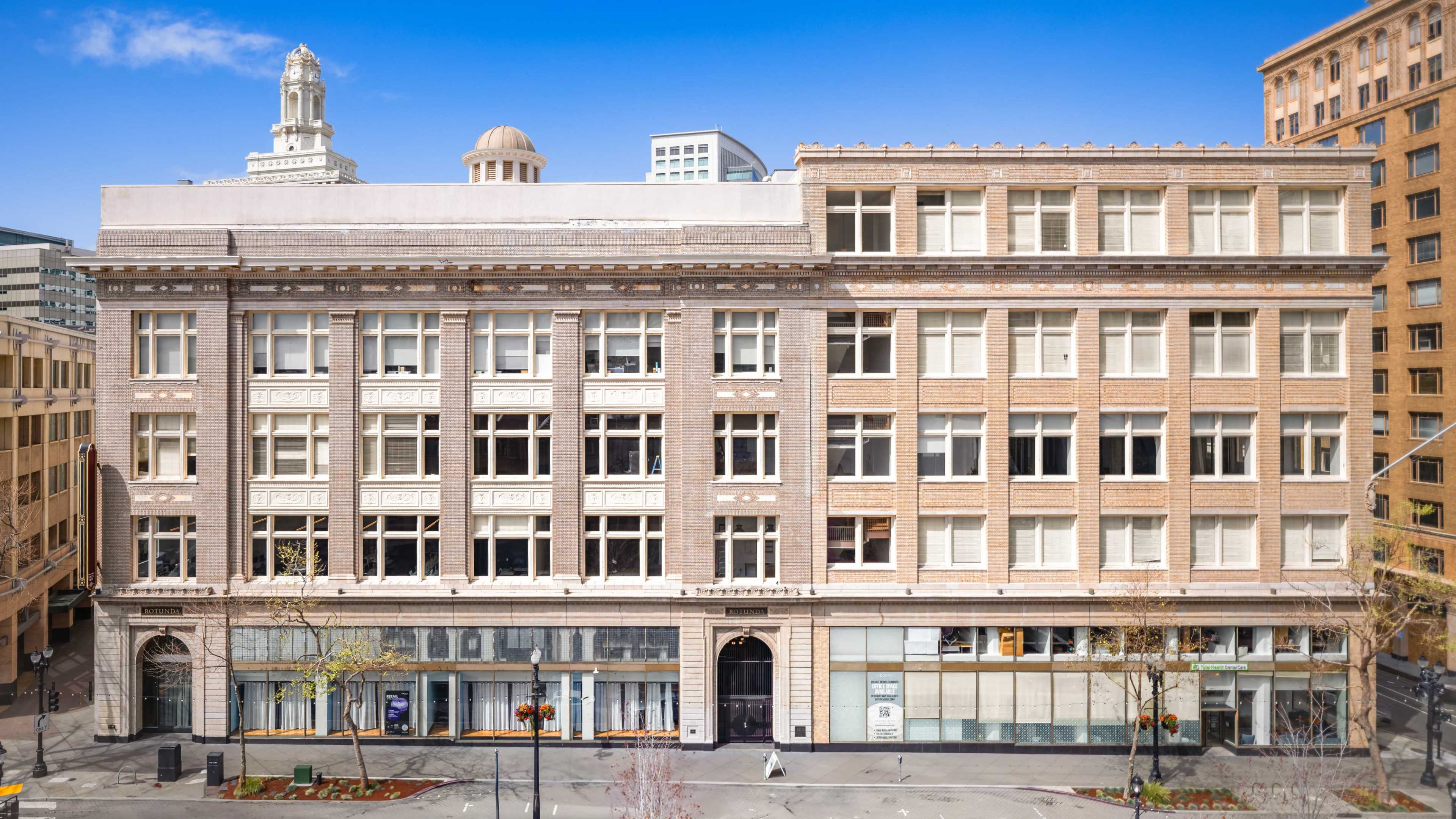 The image shows a large, historic brick building with multiple windows and a domed roof located in an urban area.