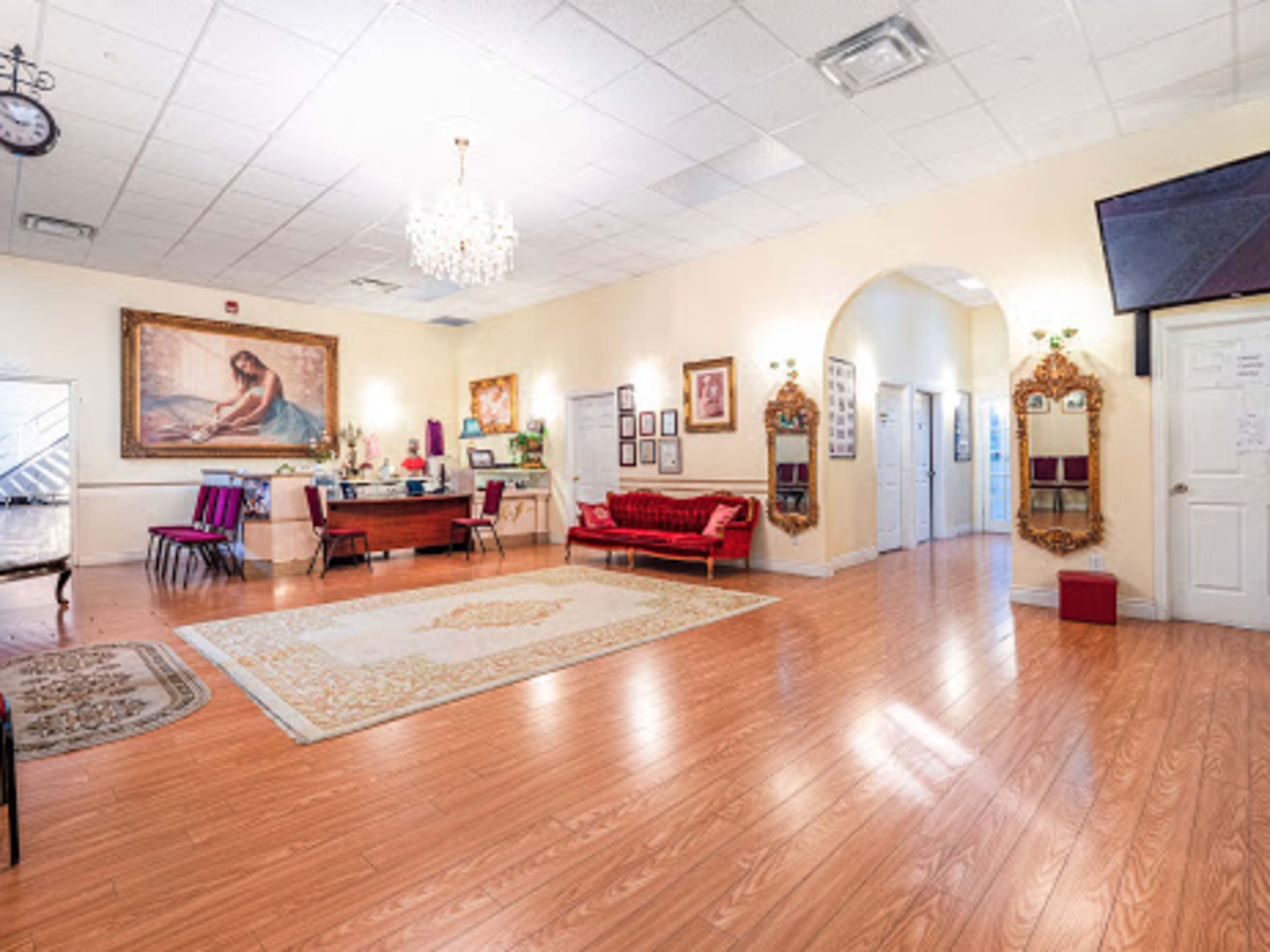 A spacious reception area with hardwood floors, a large ornate painting on the wall, a chandelier, and a mix of seating arrangements.