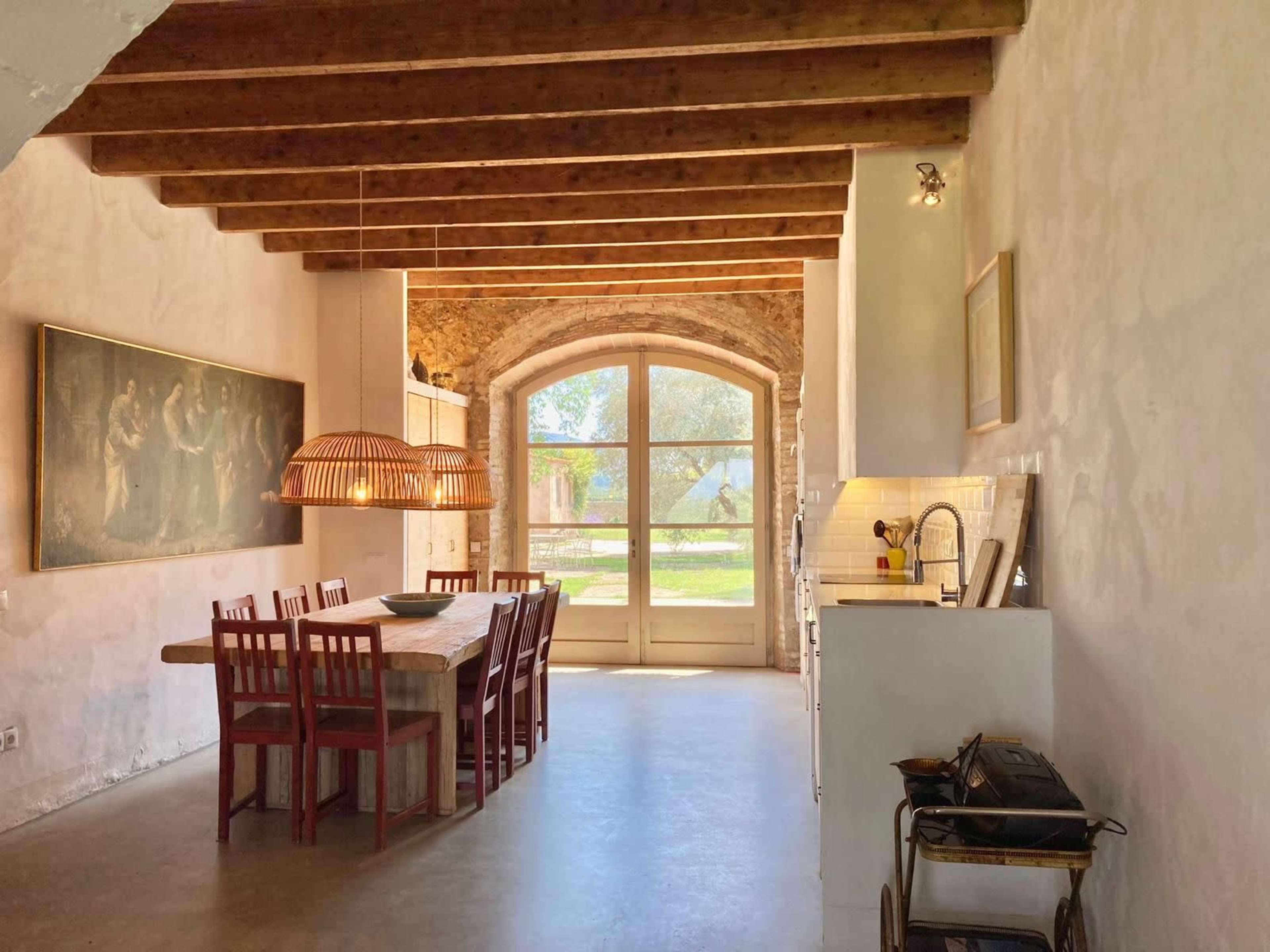 A modern kitchen and dining area with a wooden table, chairs, and large windows that provide a view of the outdoors.