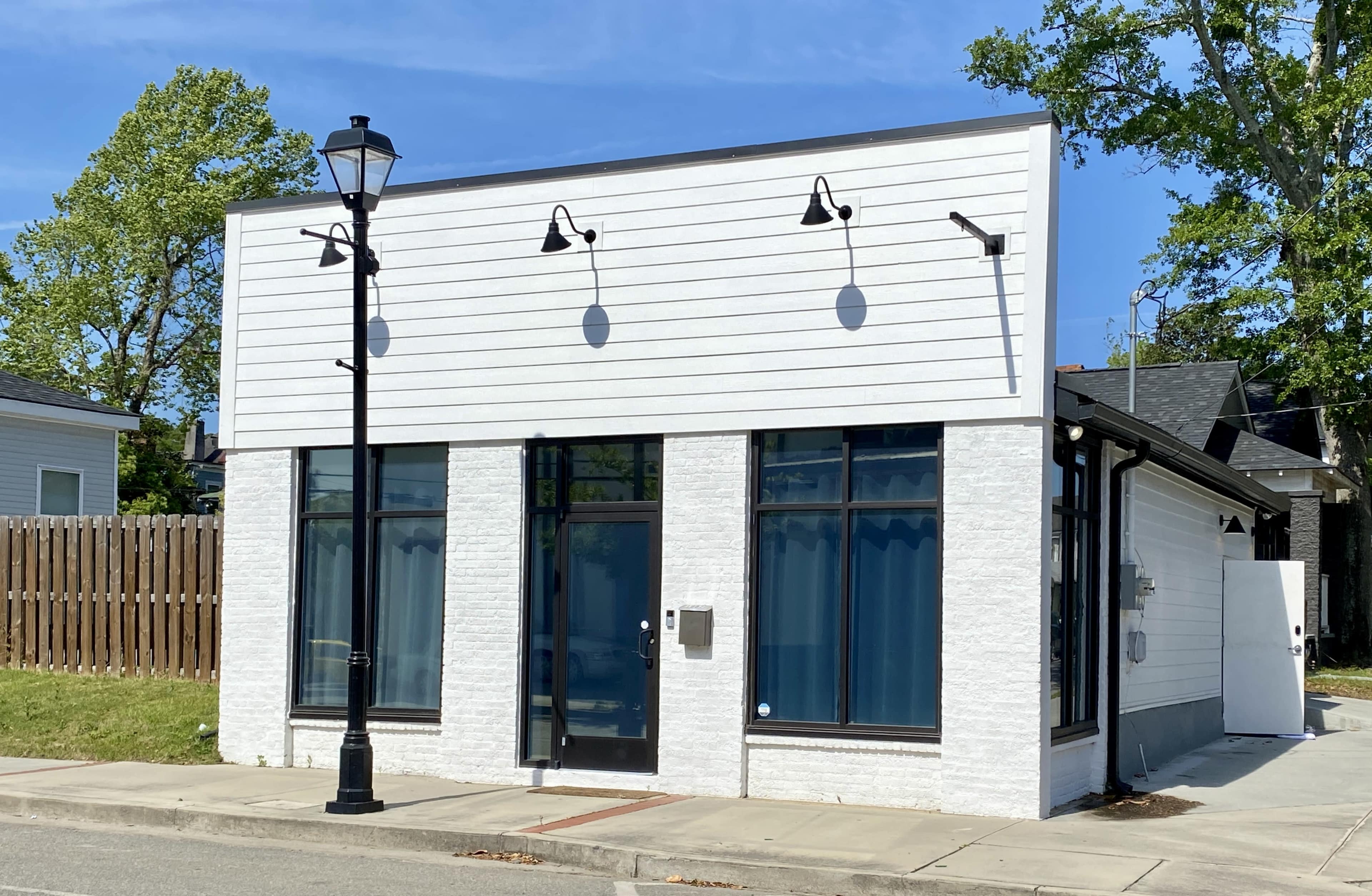 A single-story commercial building with a white exterior and large windows sits at the corner of a quiet street, alongside a decorative street lamp.