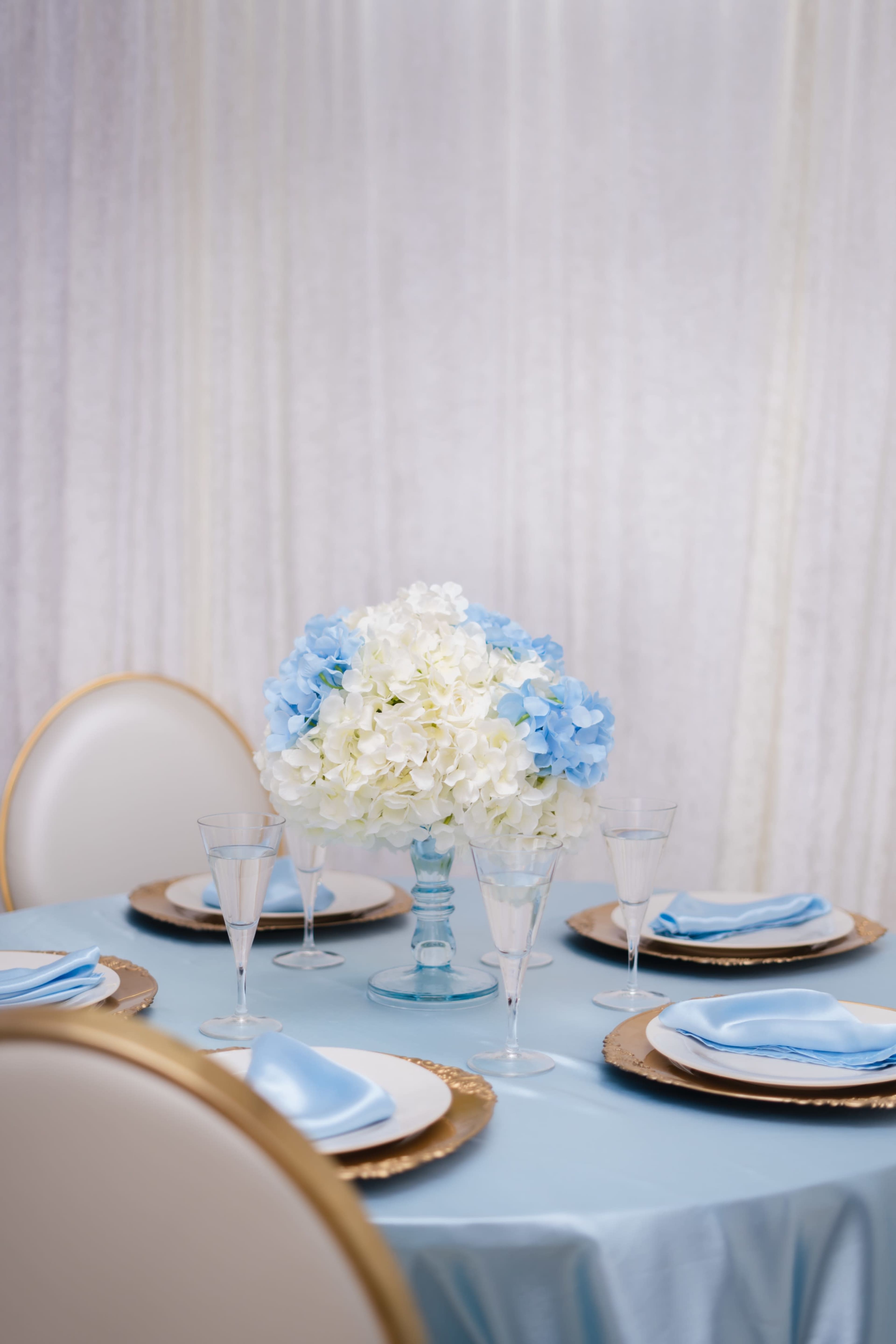 A set dining table is adorned with blue and white floral centerpieces, elegant glassware, and neatly arranged plates.