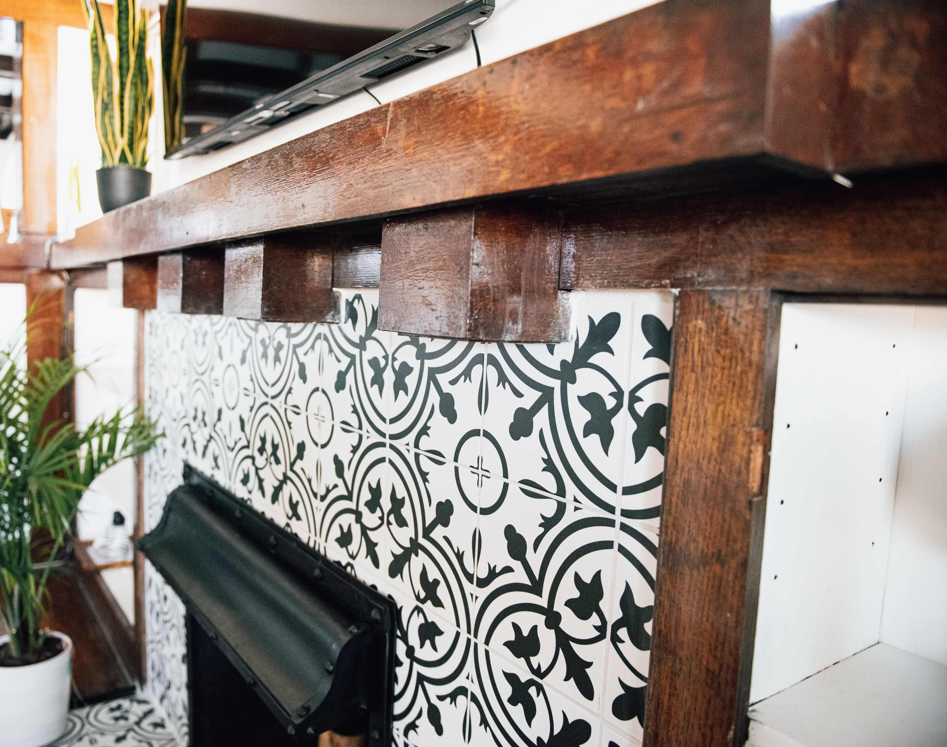 A wooden mantelpiece above a tiled fireplace, featuring black and white patterned tiles.