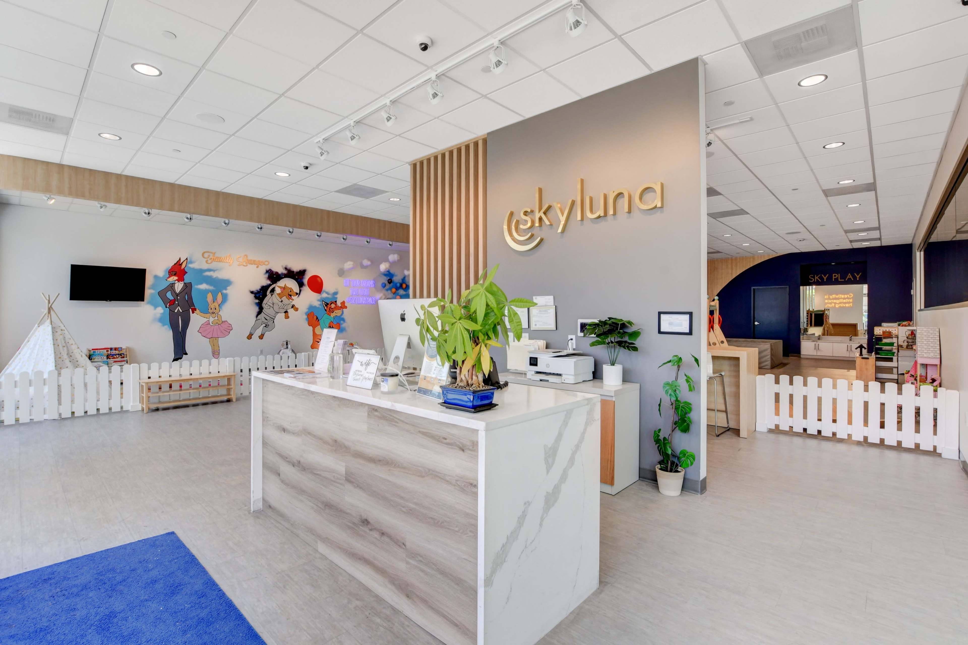 A modern reception area with a desk, decorative wall art, and play zones in a brightly lit space.