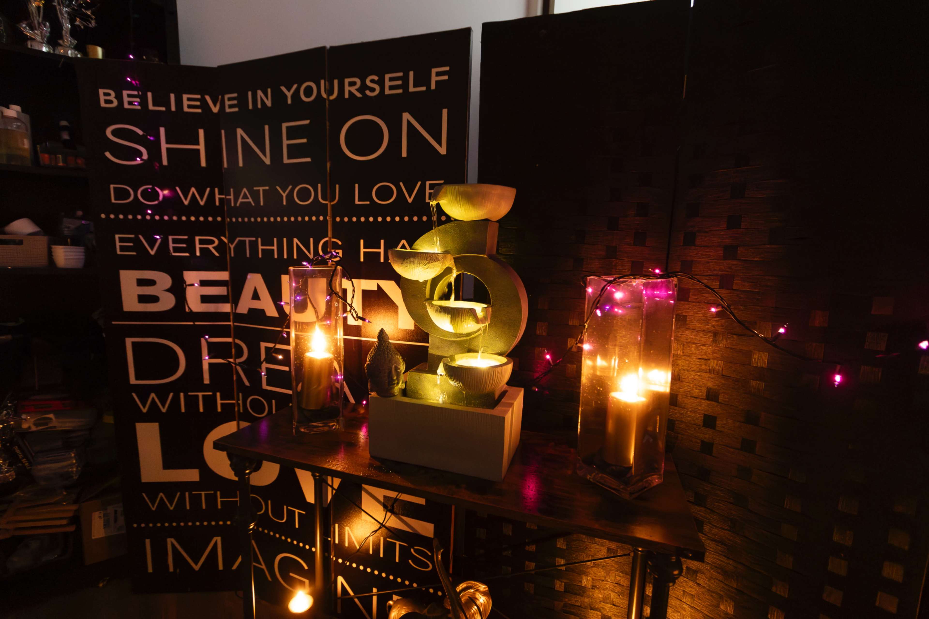 The scene features a table with decorative candles and a small fountain, set against a backdrop of motivational quotes and dim lighting.