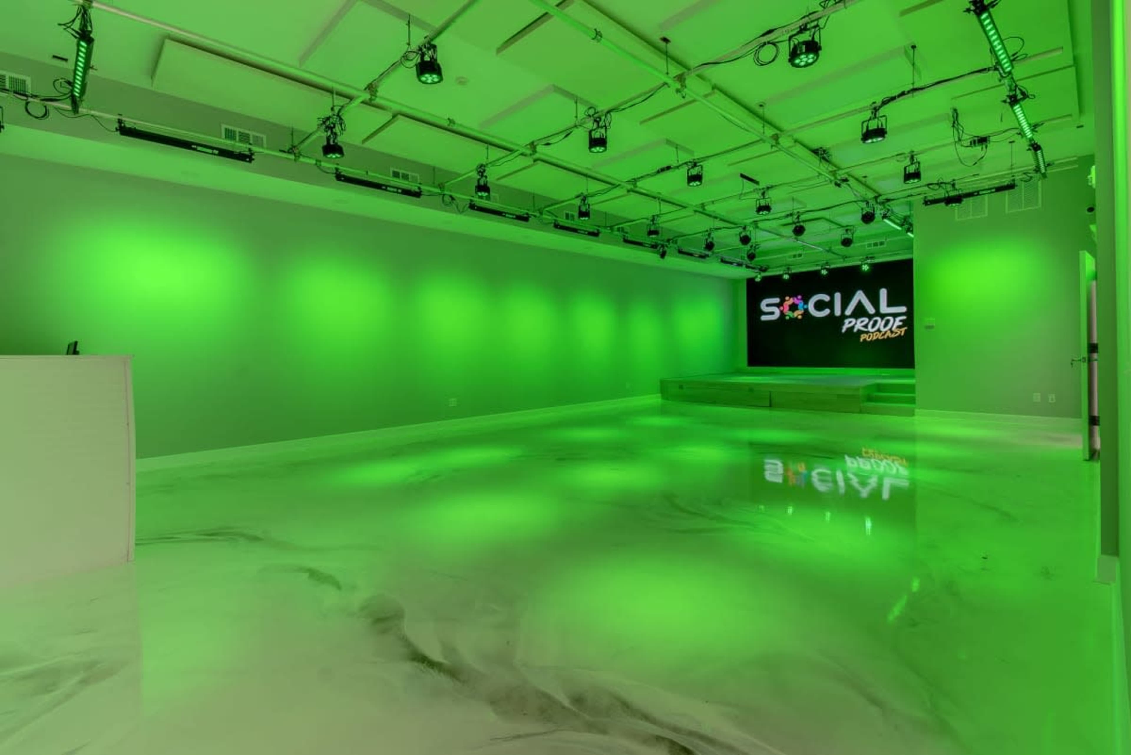 The image shows a modern, empty room with a glossy floor and green lighting, featuring a stage and a screen displaying the text "SOCIAL PRO".