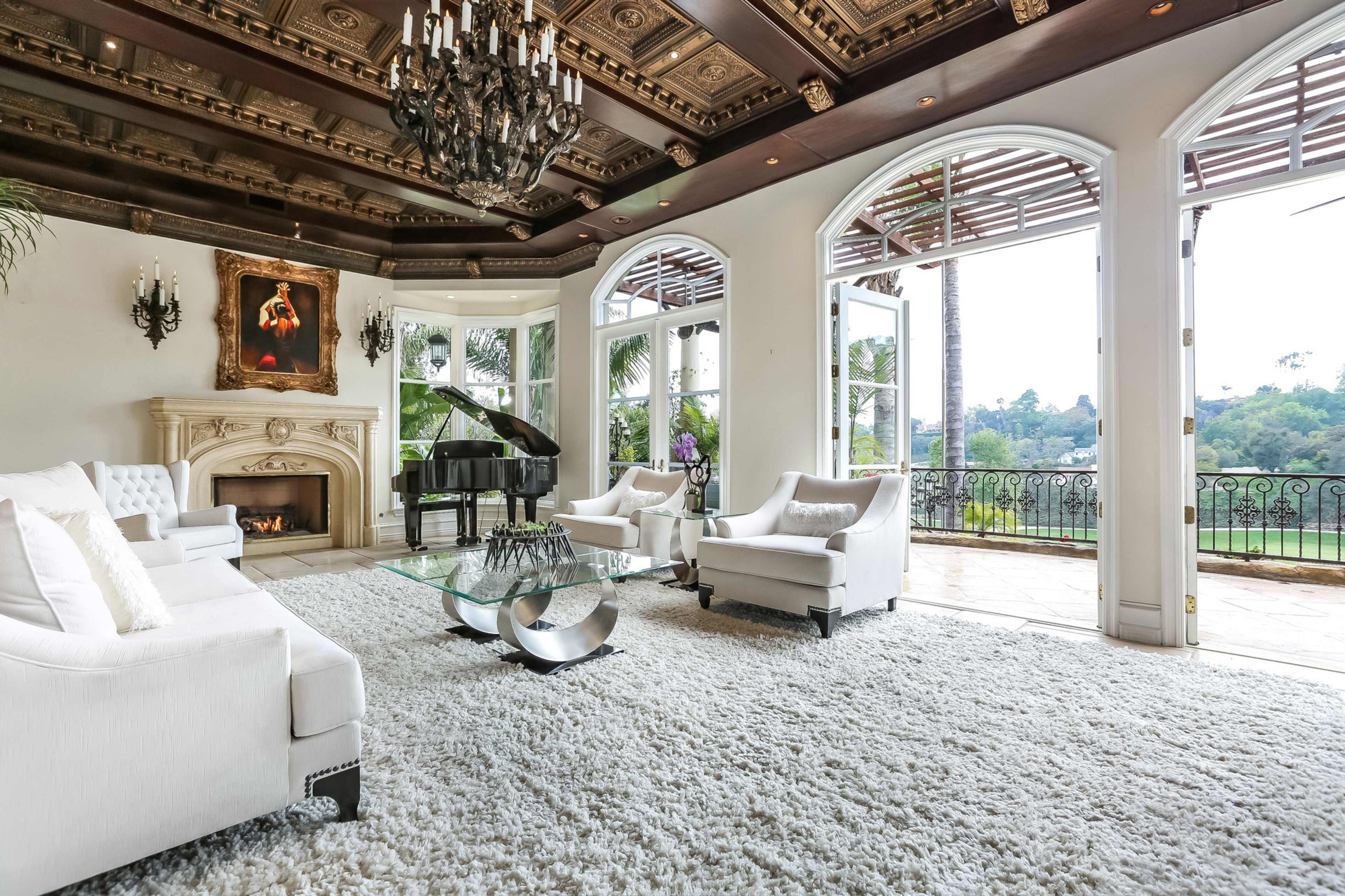 An elegantly furnished living room with a grand piano, a fireplace, and large windows offering a view of the outdoors.