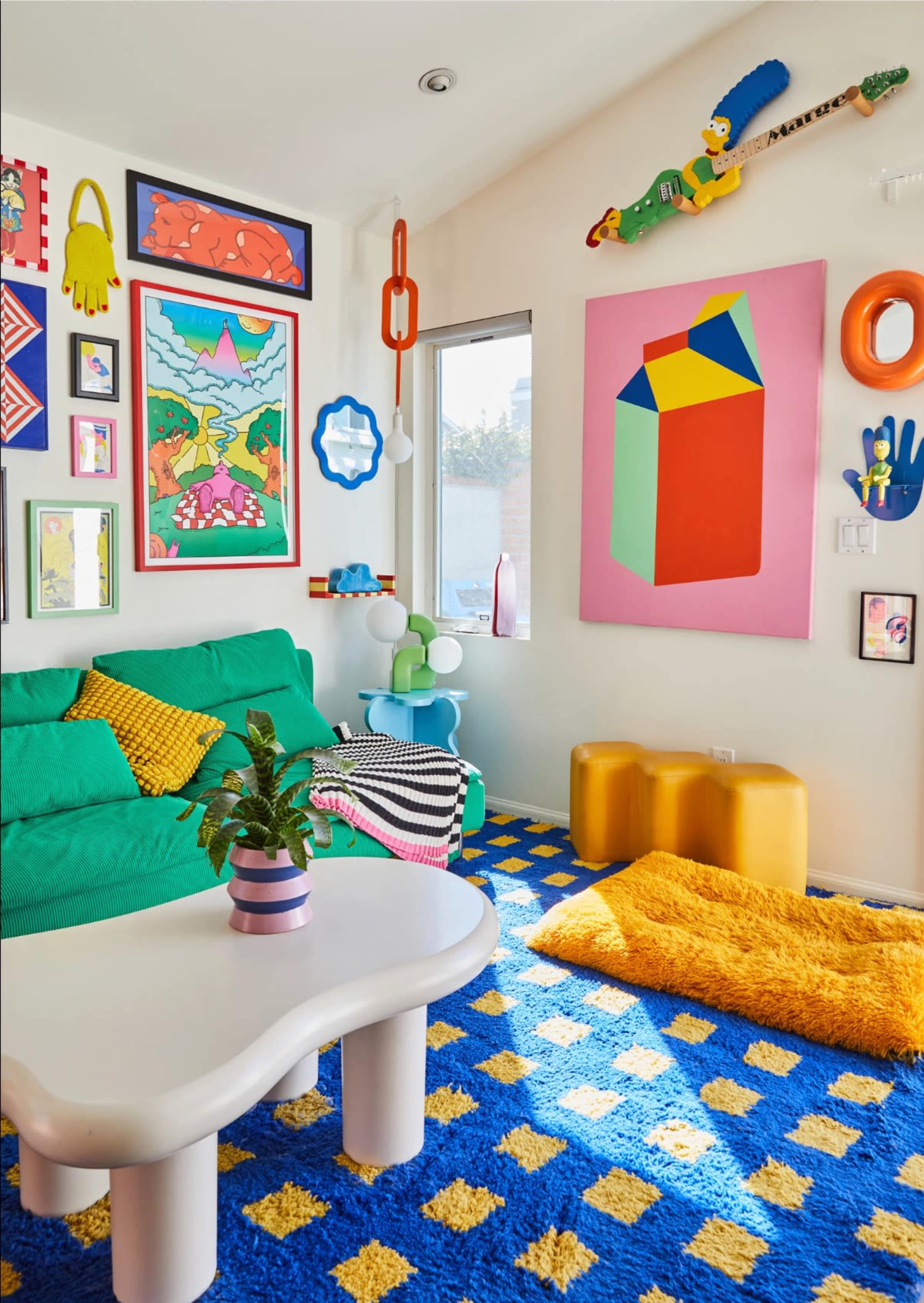The room features a colorful decor with a green sofa, vibrant artwork on the walls, and a patterned blue rug.
