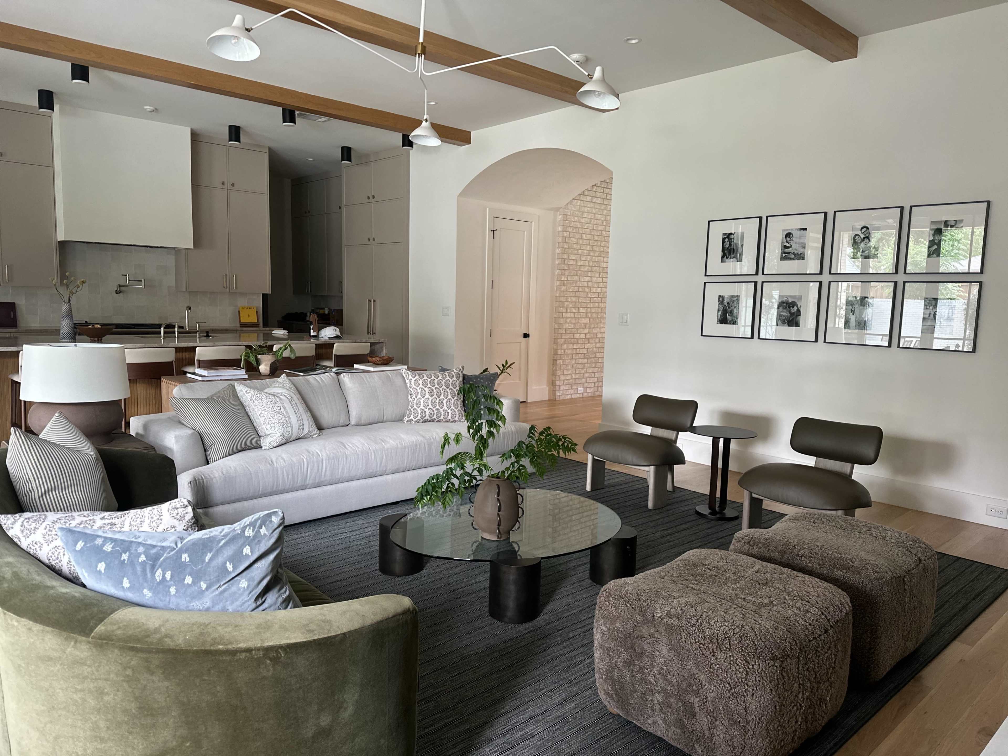 The image shows a modern living room with a large sofa, two chairs, a coffee table, and a gallery wall featuring framed black-and-white photos.