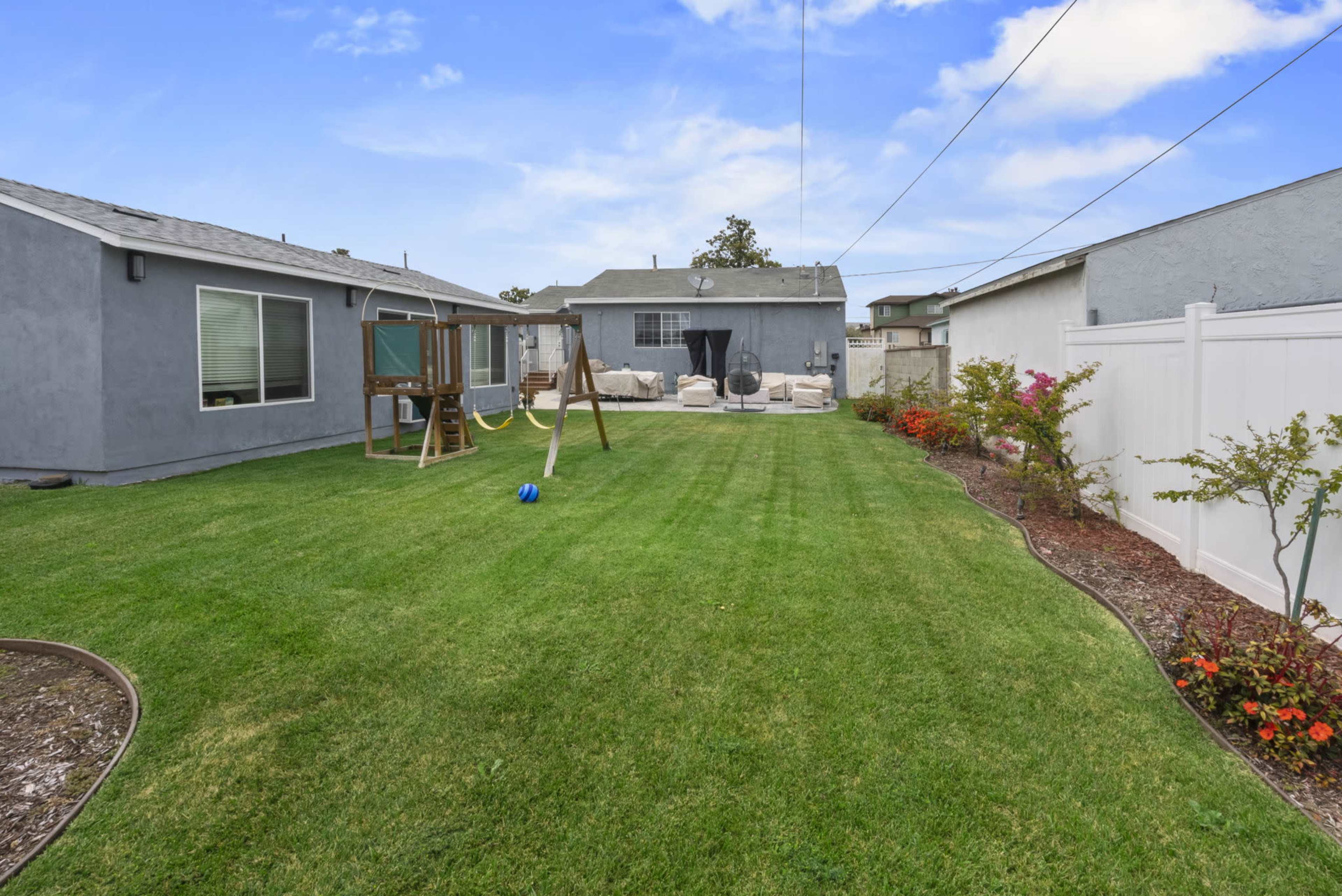 The image shows a backyard with a well-maintained lawn, a swing set, and patio furniture in a residential setting.
