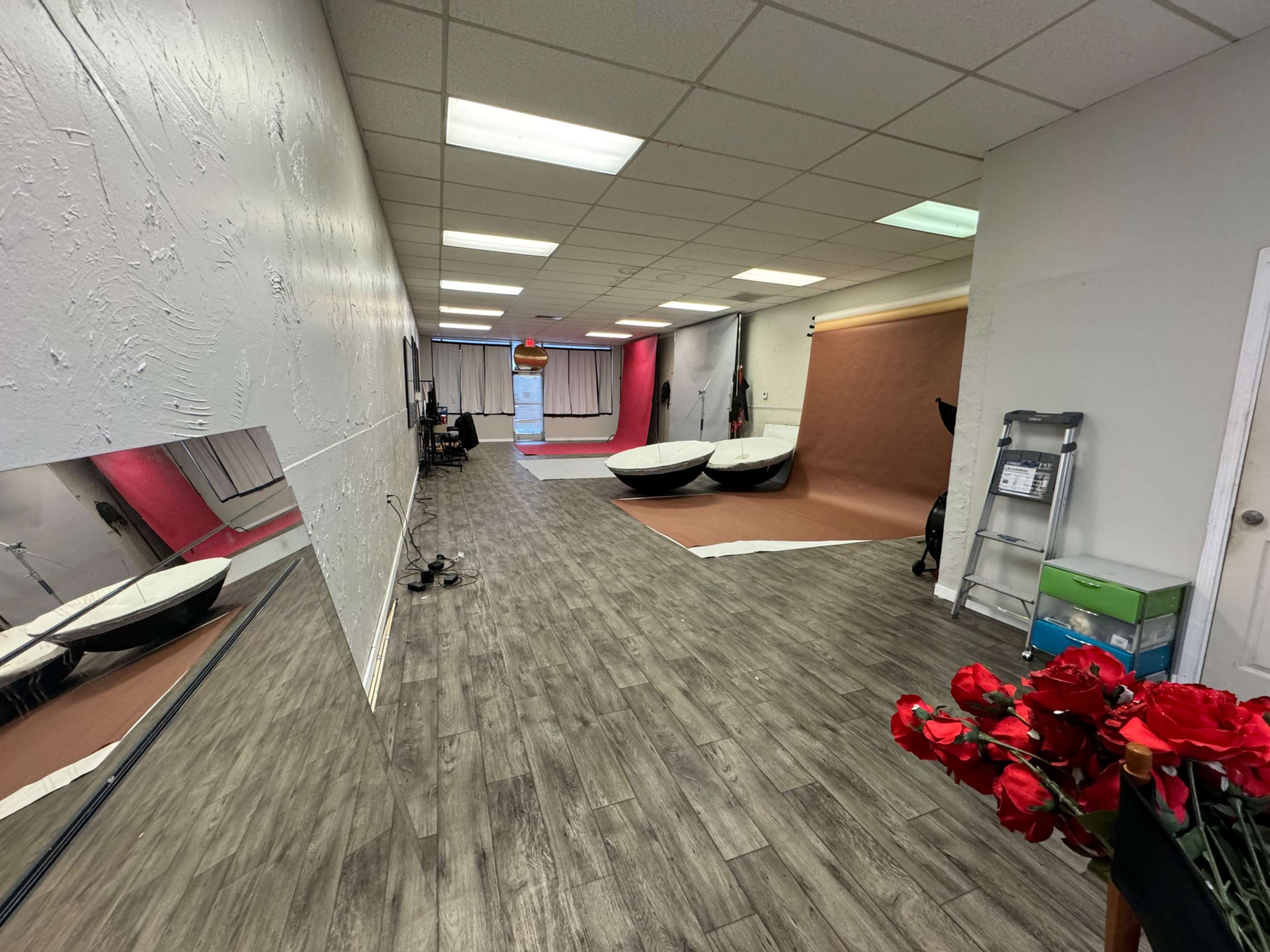 A spacious photography studio with a textured wall, wooden flooring, and various backdrops set up for shoots.