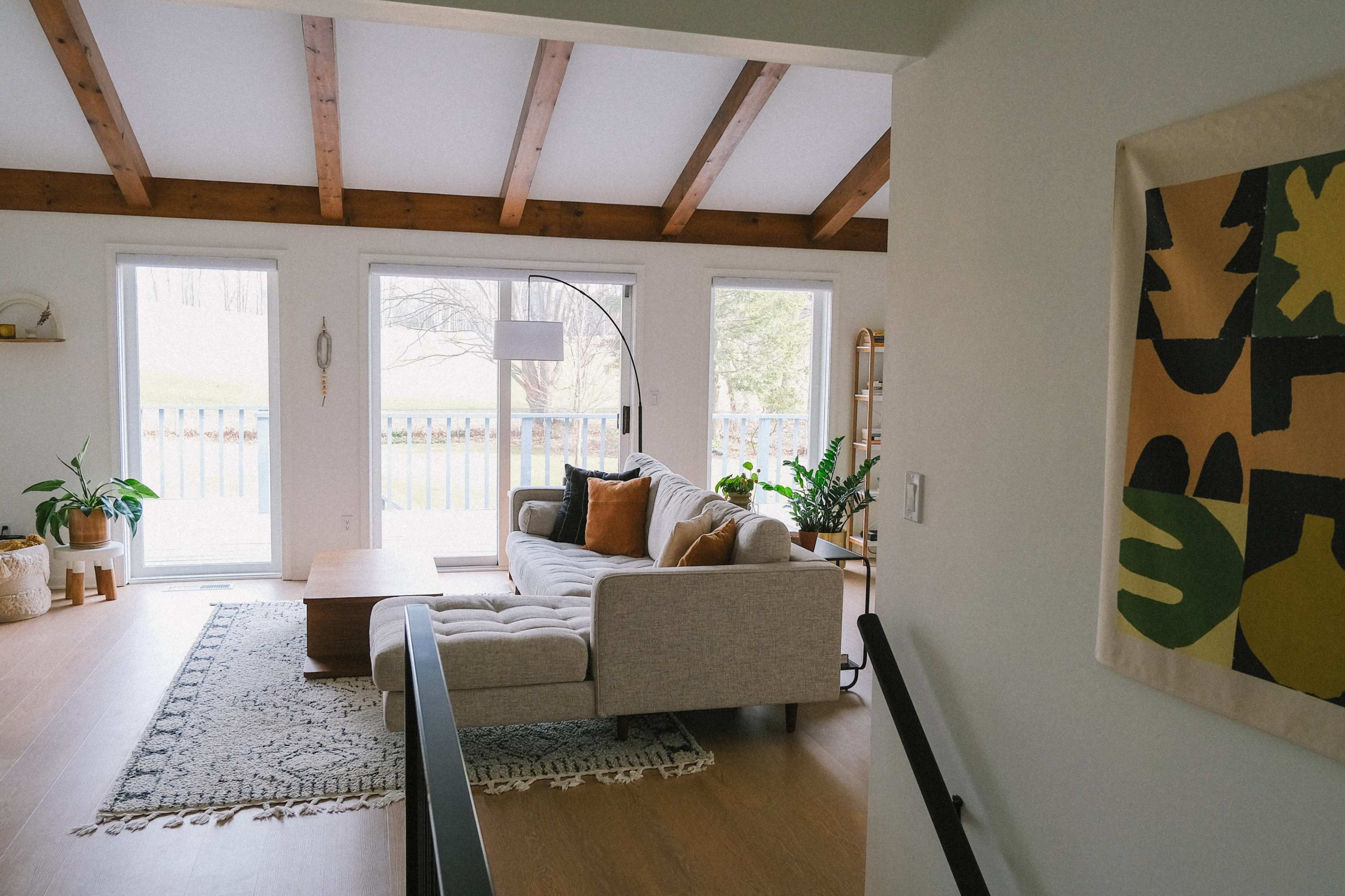 A bright living room features a sectional sofa, wooden coffee table, and large windows overlooking a green landscape.