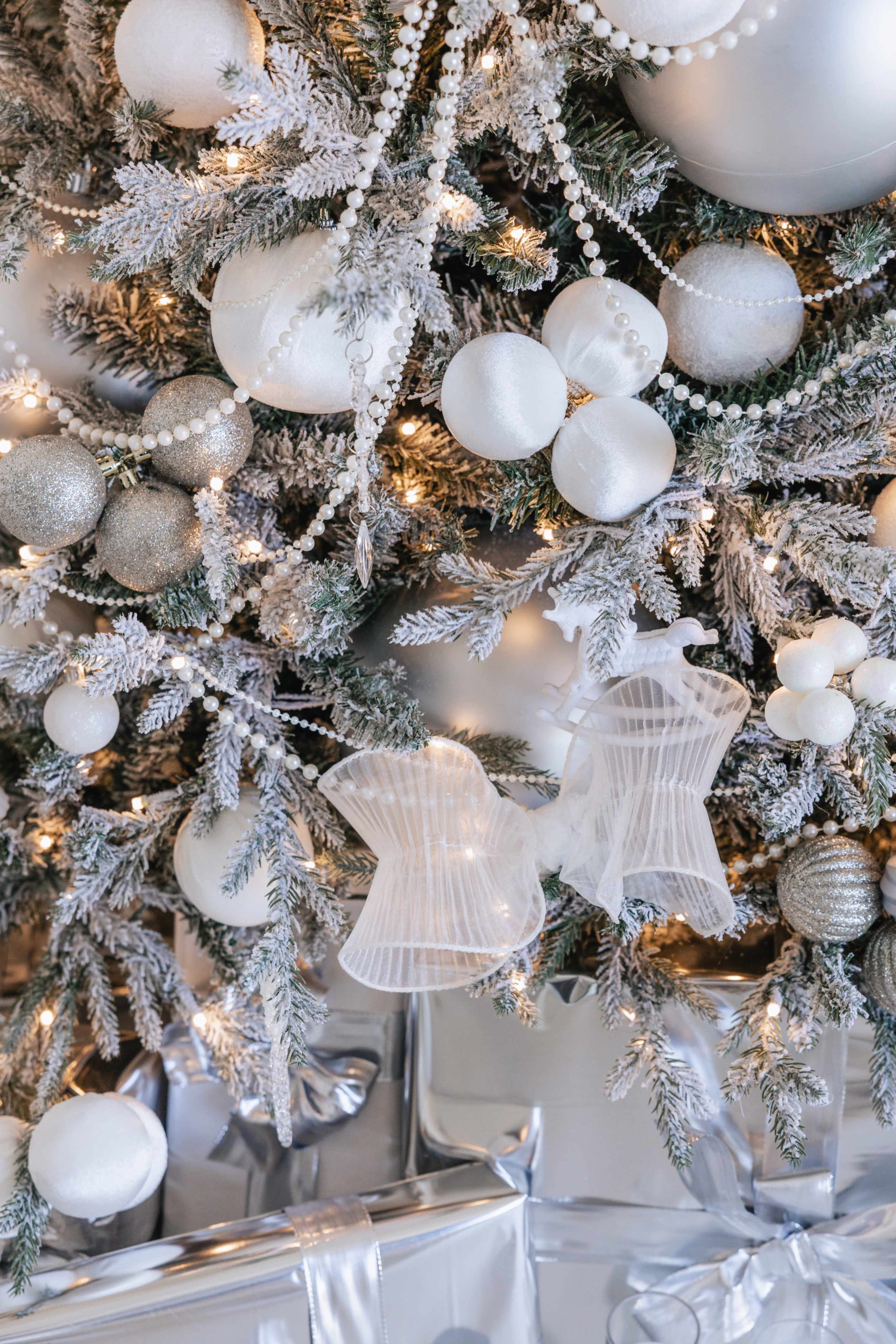 The image shows a decorated Christmas tree with white and silver ornaments, sparkling lights, and wrapped gifts underneath.