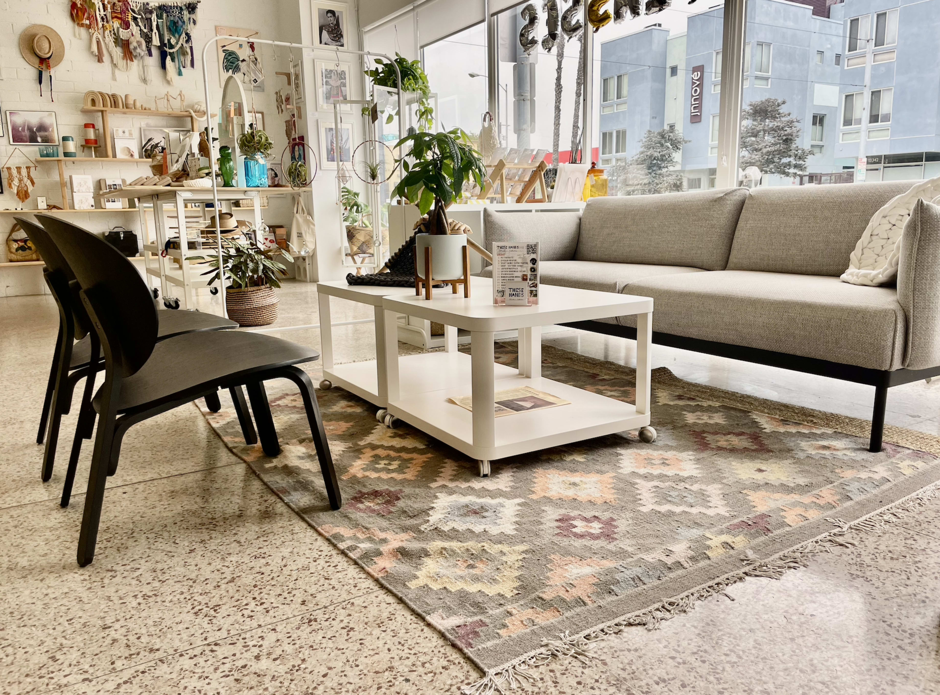 A modern interior space features a gray sofa, a coffee table on a patterned rug, and black chairs arranged around the seating area.