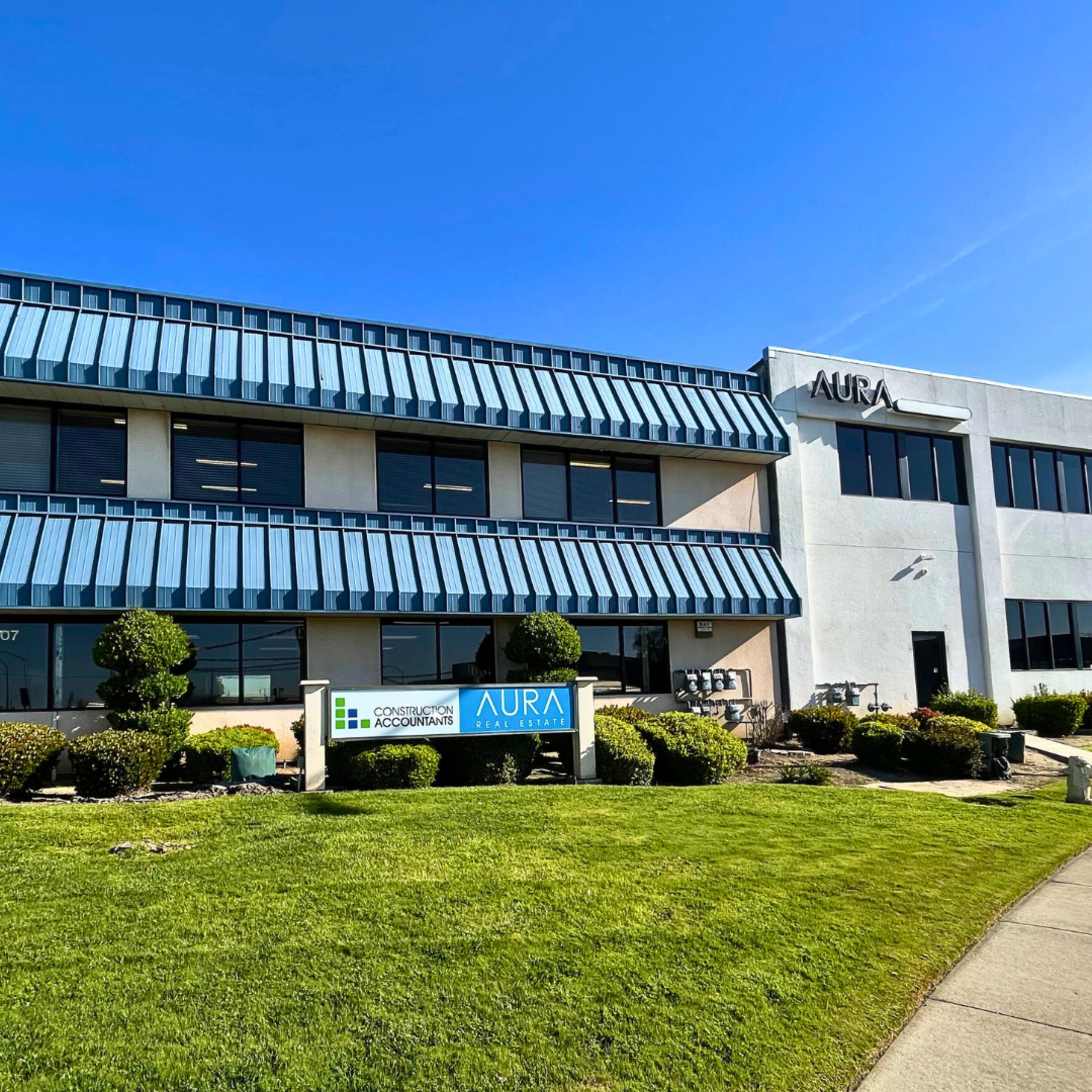 A two-story office building with a blue awning and signage for AURA and a accounting firm.