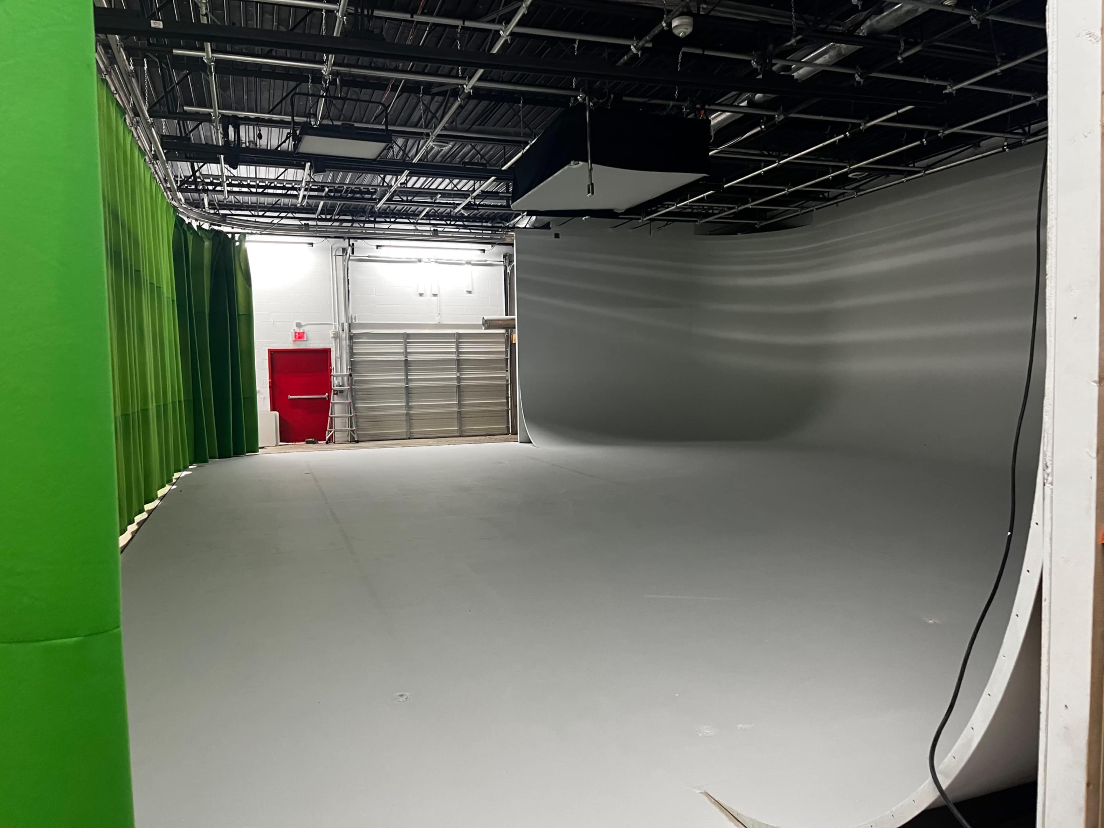 The image shows an empty studio with a gray floor and green curtains on one side.