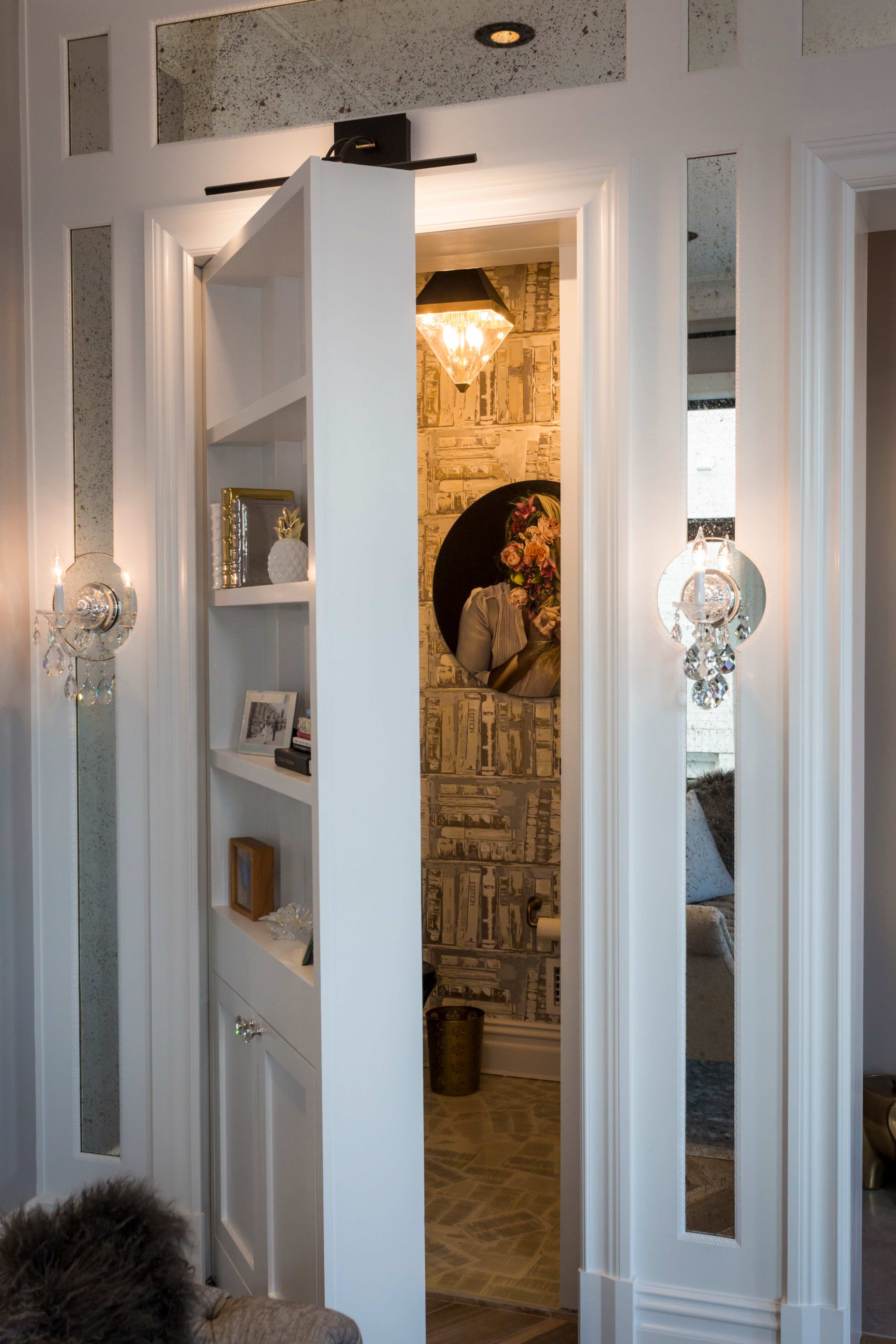 A sliding bookshelf door opens to reveal a well-decorated room with patterned wallpaper and a decorative light fixture.