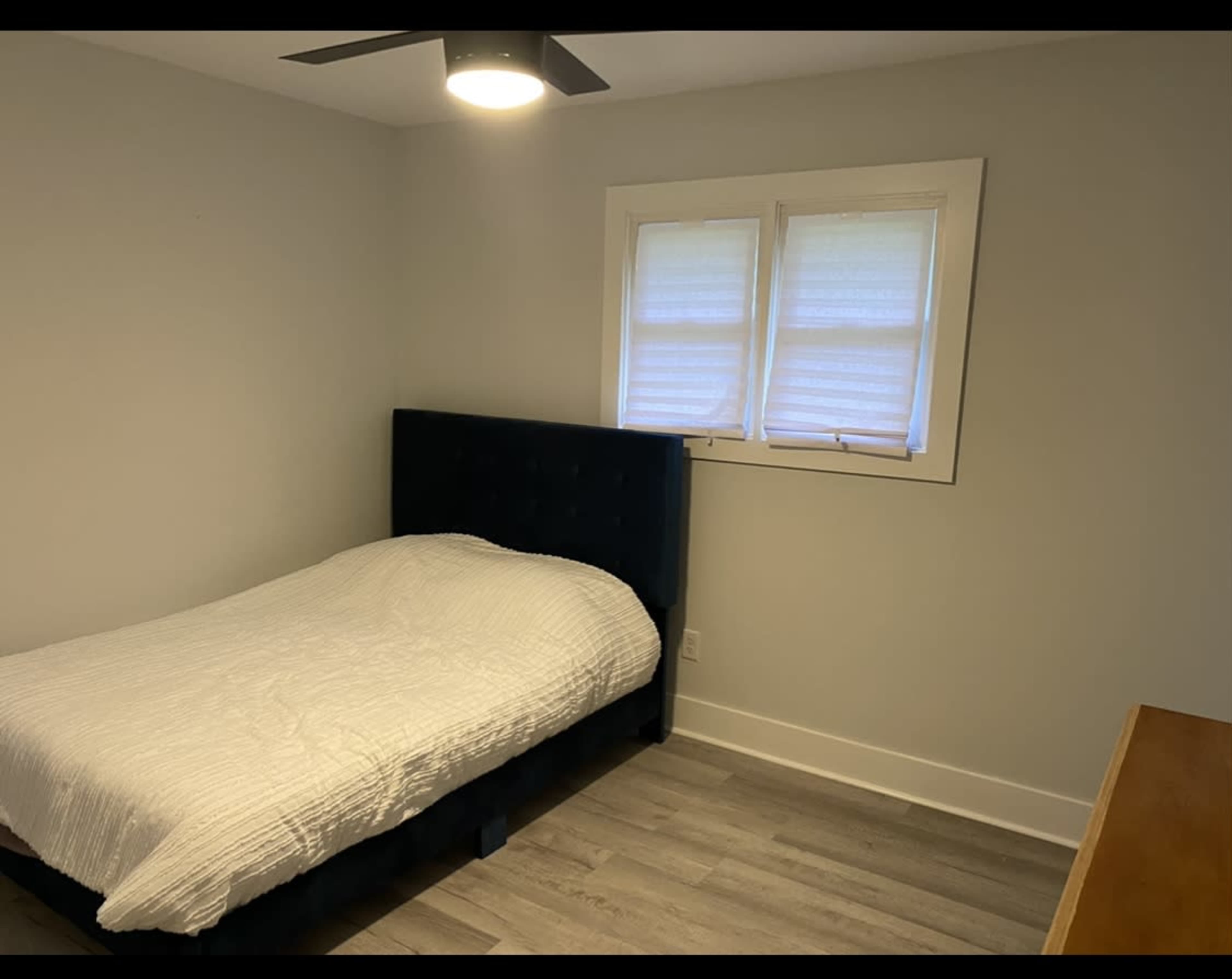 A simple bedroom with a bed covered by a white quilt and two windows on the wall.