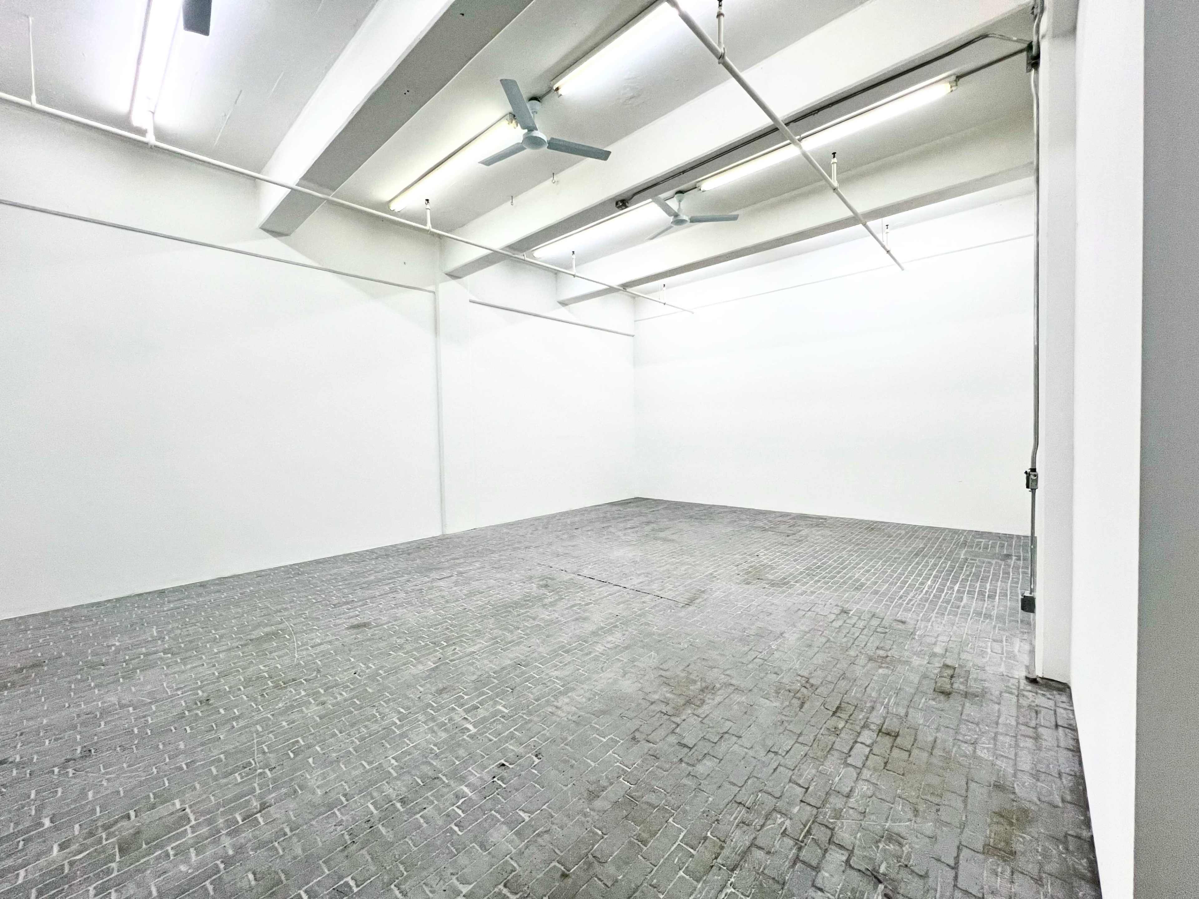An empty, well-lit interior space with white walls and a gray brick floor.