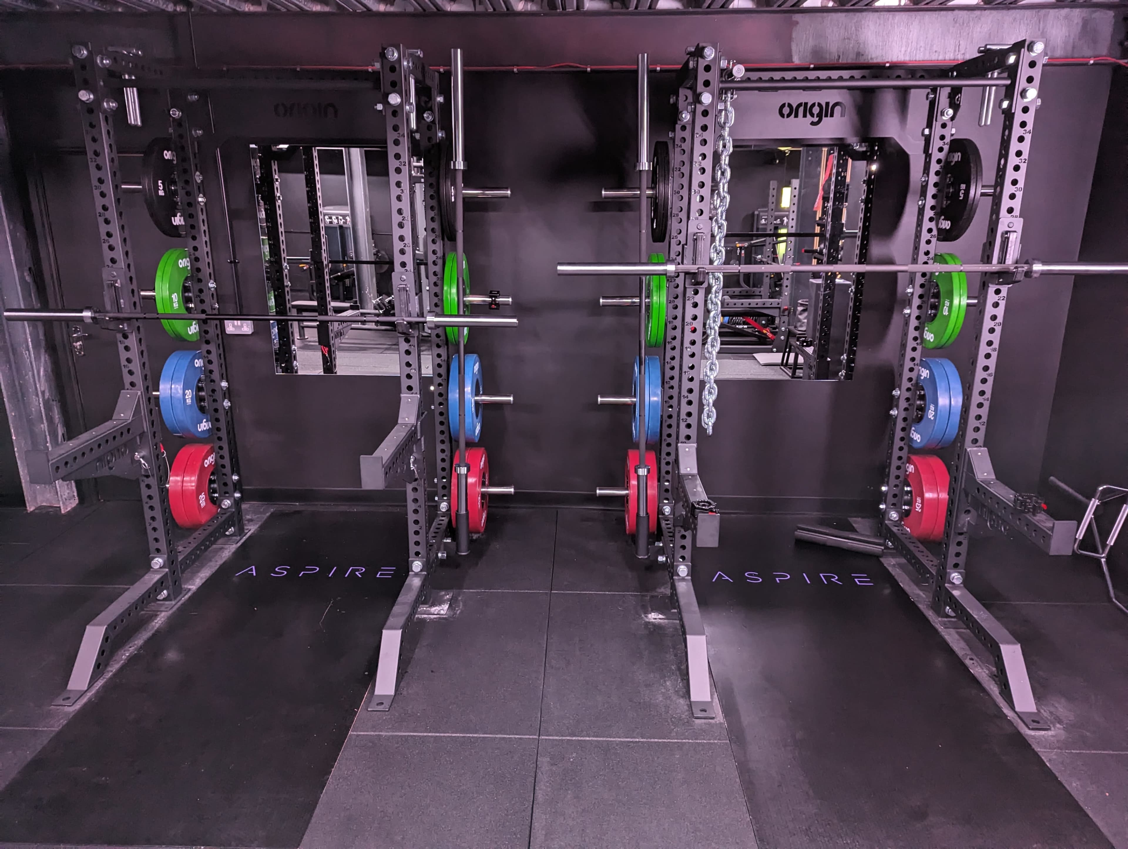 A gym area with two power racks, each equipped with colorful weight plates arranged neatly on the bars.