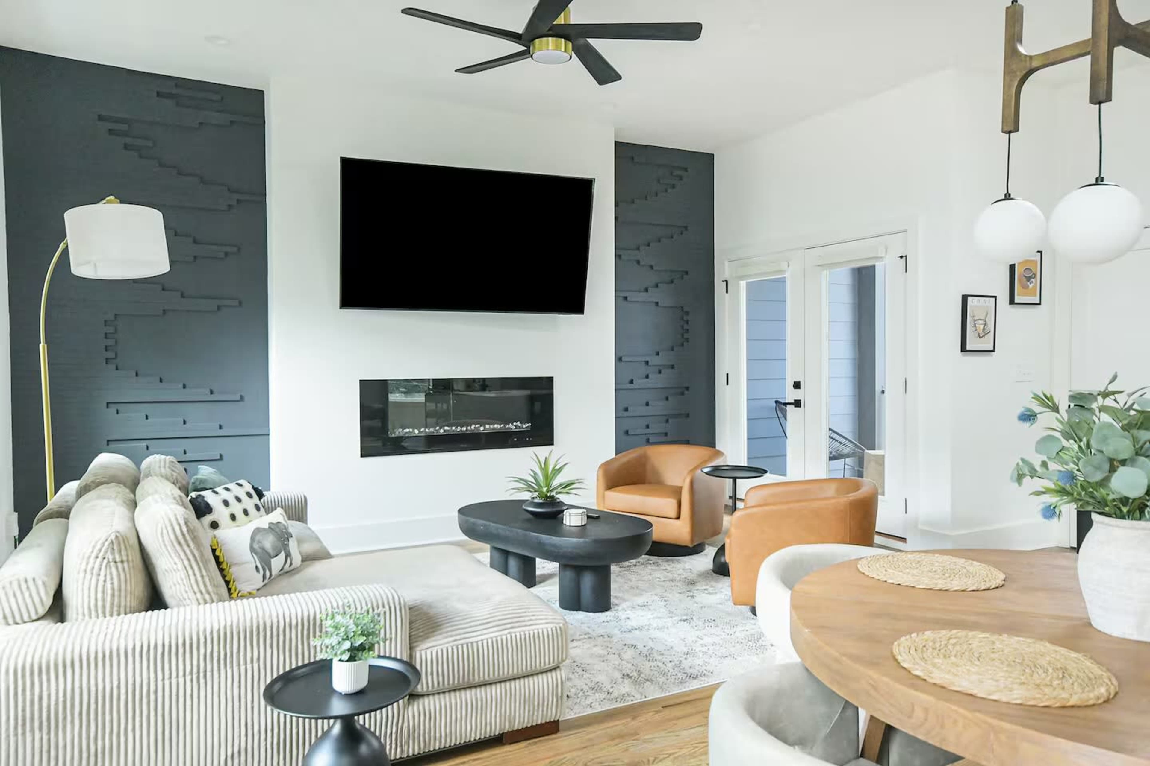 The image shows a modern living room featuring a sectional sofa, two accent chairs, a coffee table, and a fireplace beneath a mounted television.
