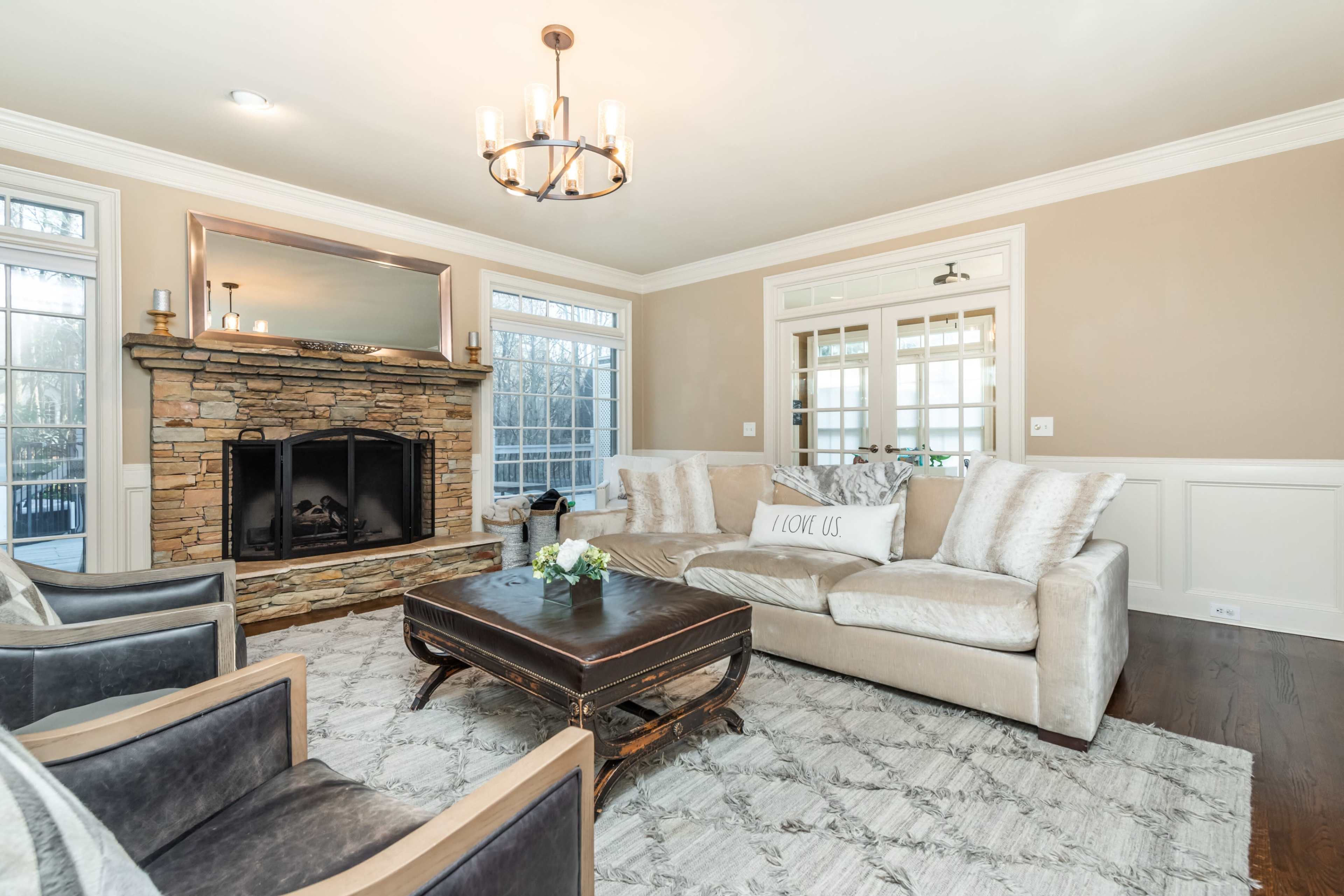 The living room features a stone fireplace, a large sectional sofa with decorative pillows, and a wooden coffee table on a patterned rug.