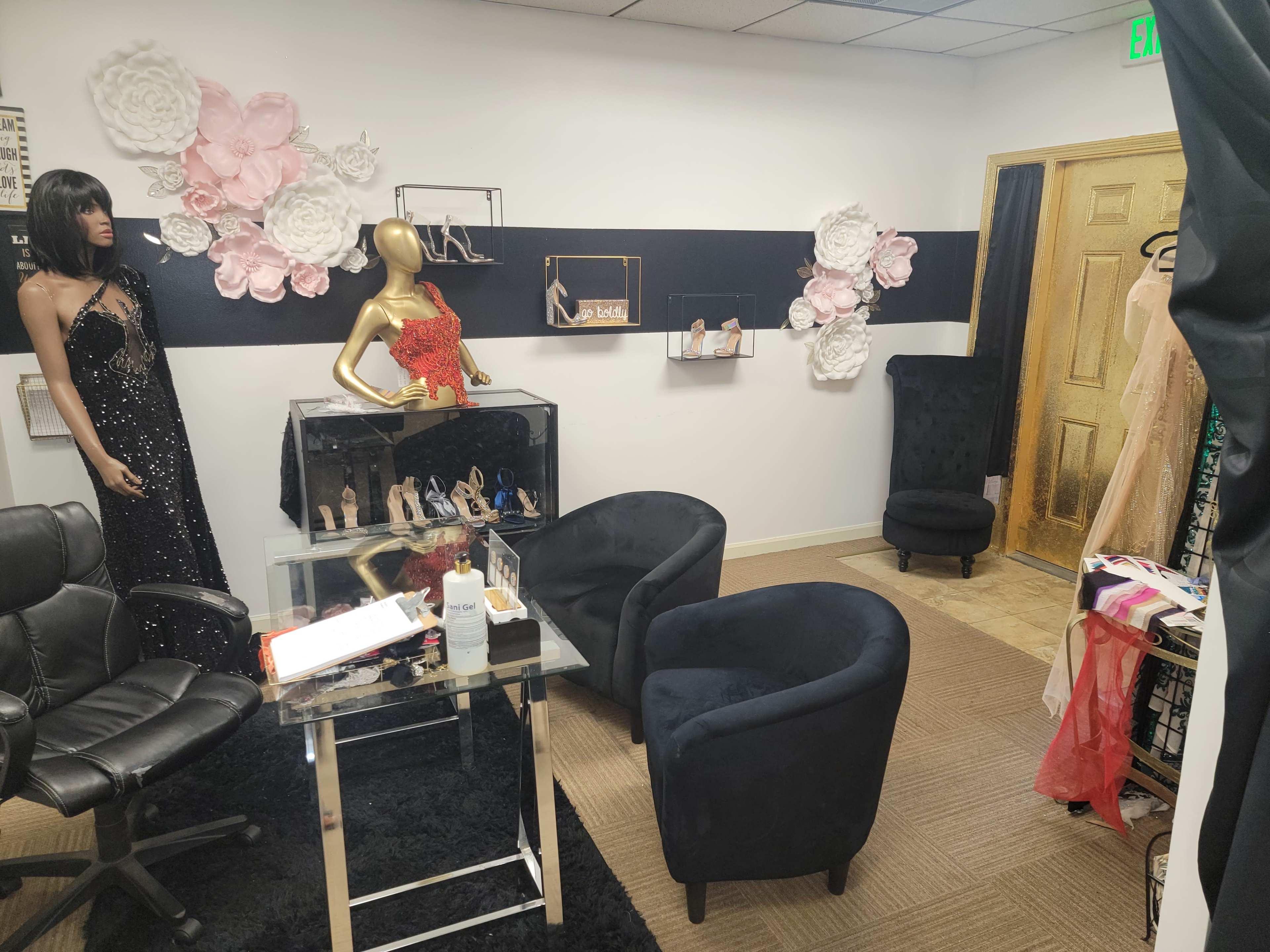 A boutique interior featuring a black carpet, a seating area with two chairs, a mannequin dressed in a sequined gown, and decorative floral accents on the wall.