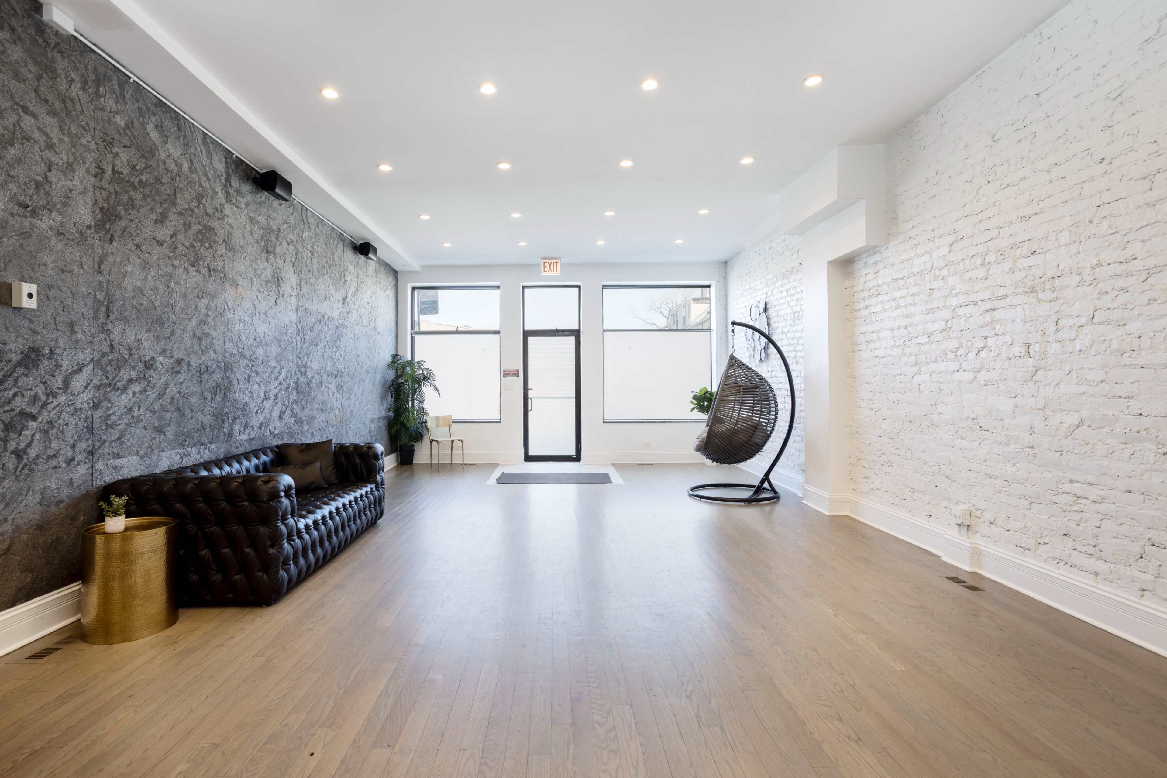 An empty, modern interior space featuring a dark leather sofa, a hanging chair, and a mix of brick and textured wall finishes.