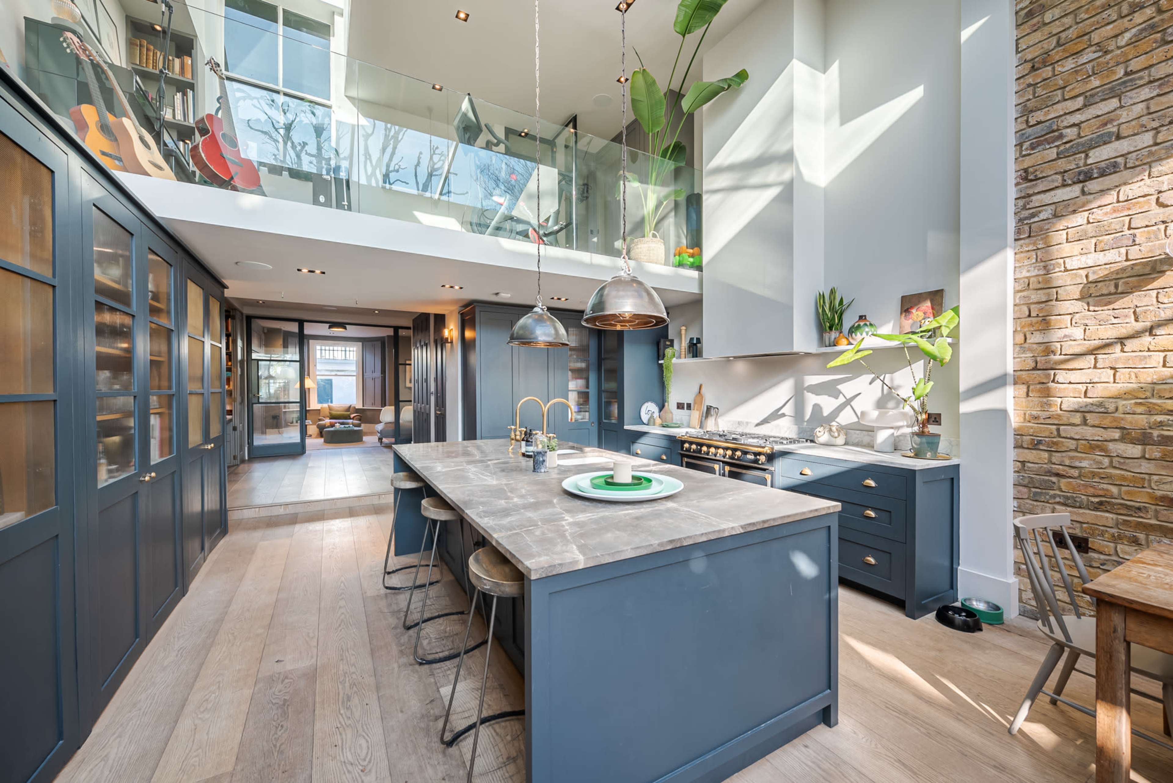 A modern kitchen with a large island, pendant lights, and glass partitions overlooking a bright living area.