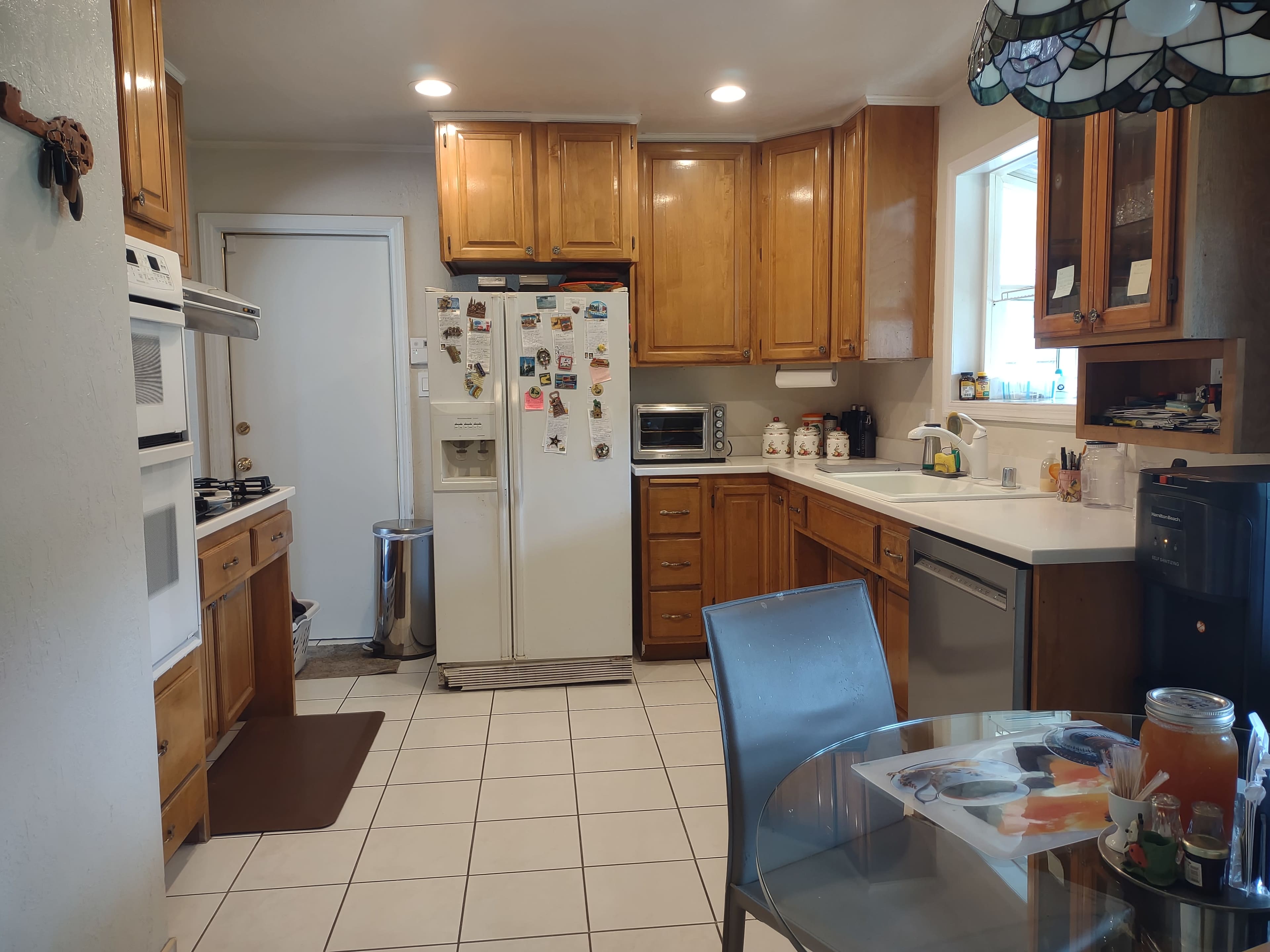 The kitchen features wooden cabinetry, white appliances, and a tiled floor with a round glass table set for dining.