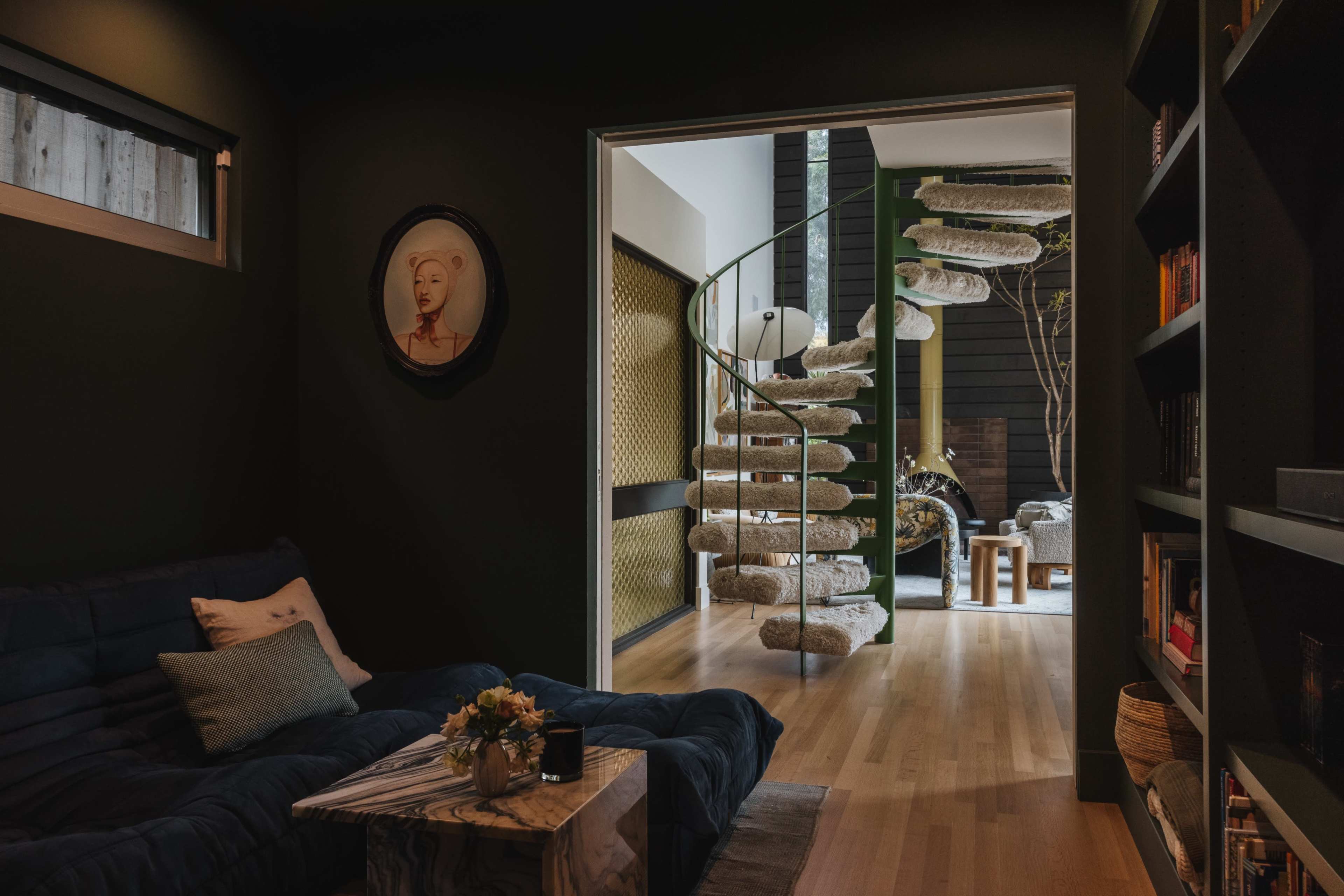 The image shows a dark room with a circular staircase made of stone-like steps leading to a brightly lit area that features plants and furniture.